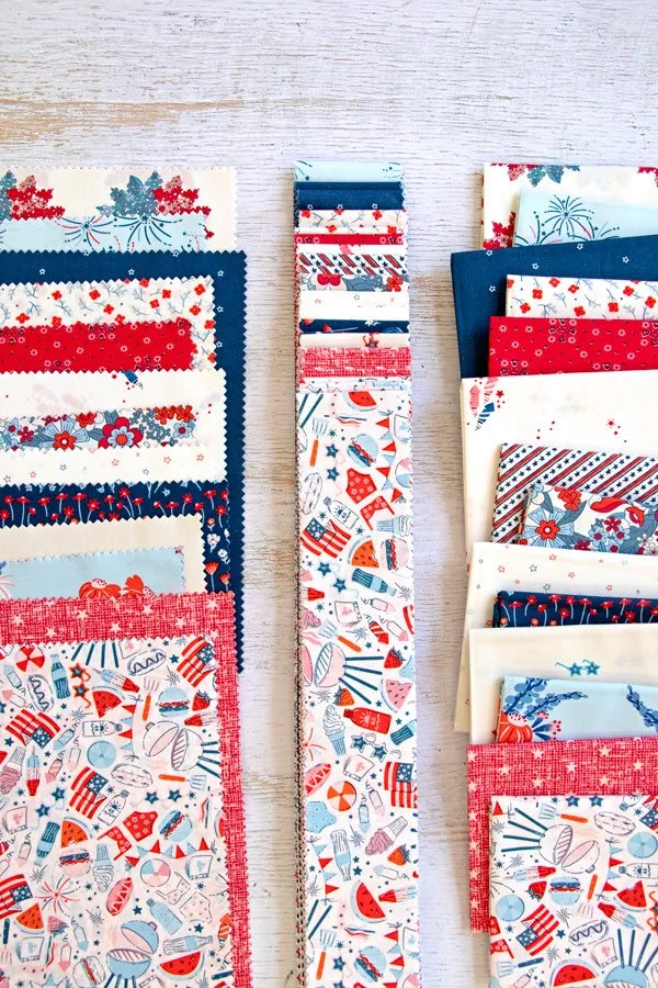 Fabrics with patriotic and summer-themed patterns in red, white, and blue, arranged in rows on a light wooden surface.