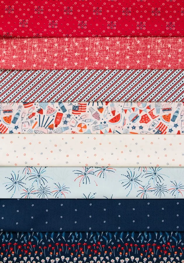 Stacked patriotic-themed fabric with red, white, and blue patterns including snowflakes, stars, stripes, fireworks, and summer motifs.
