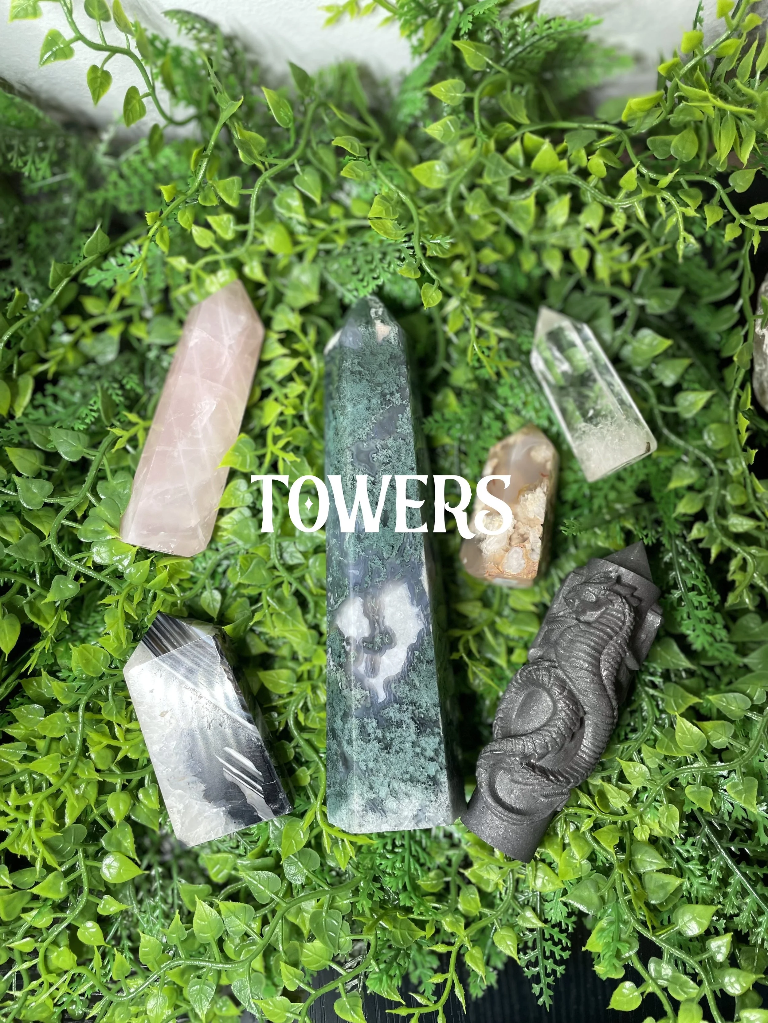 Various colorful stones and crystal points arranged on green foliage with the word TOWERS overlaid.