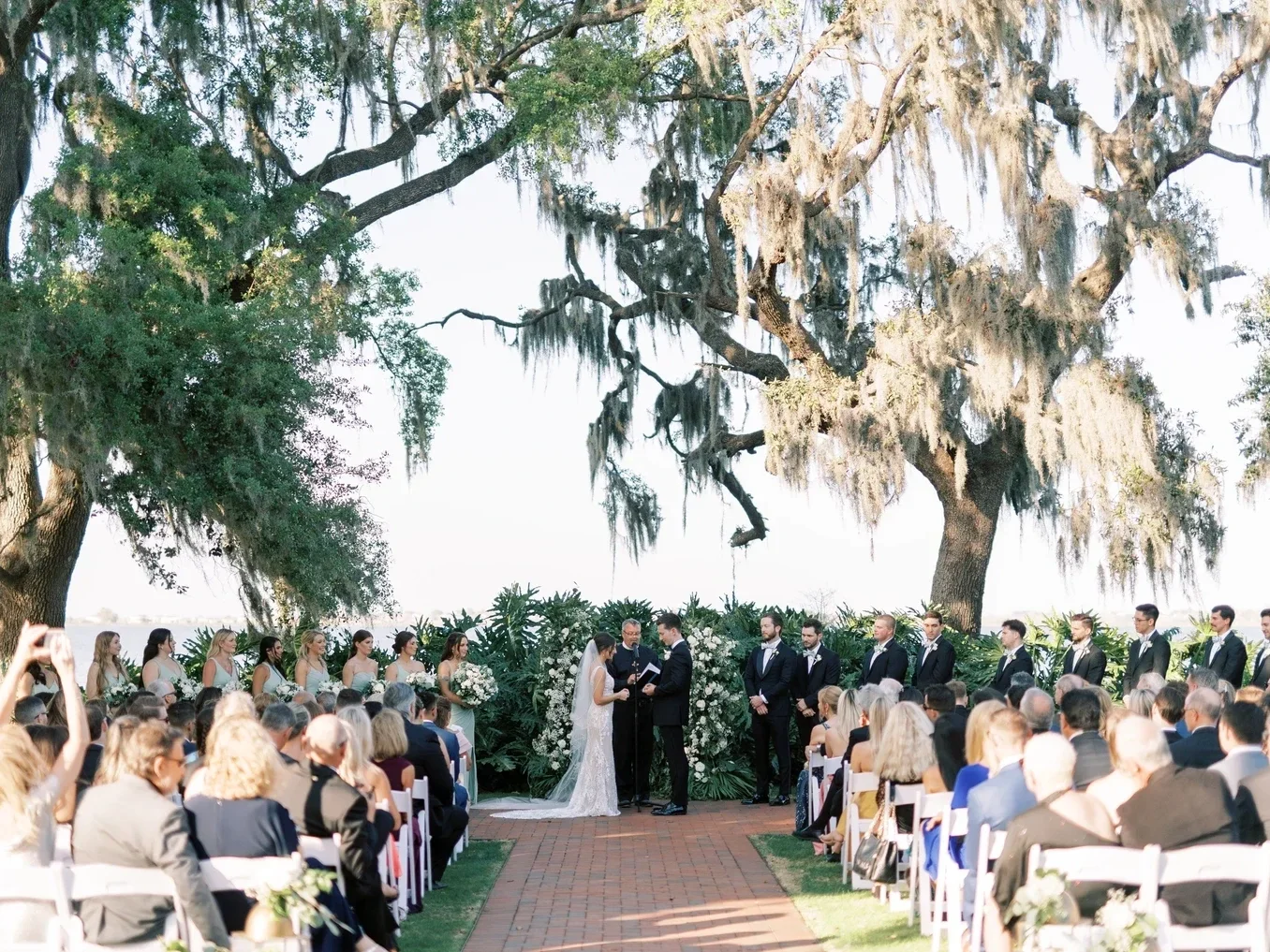 You’ll say “I do” beneath the canopy of live oaks, then move with your guests to the Estate House and Terrace for cocktail hour, where glowing string lights and lake breezes set the tone for the evening.