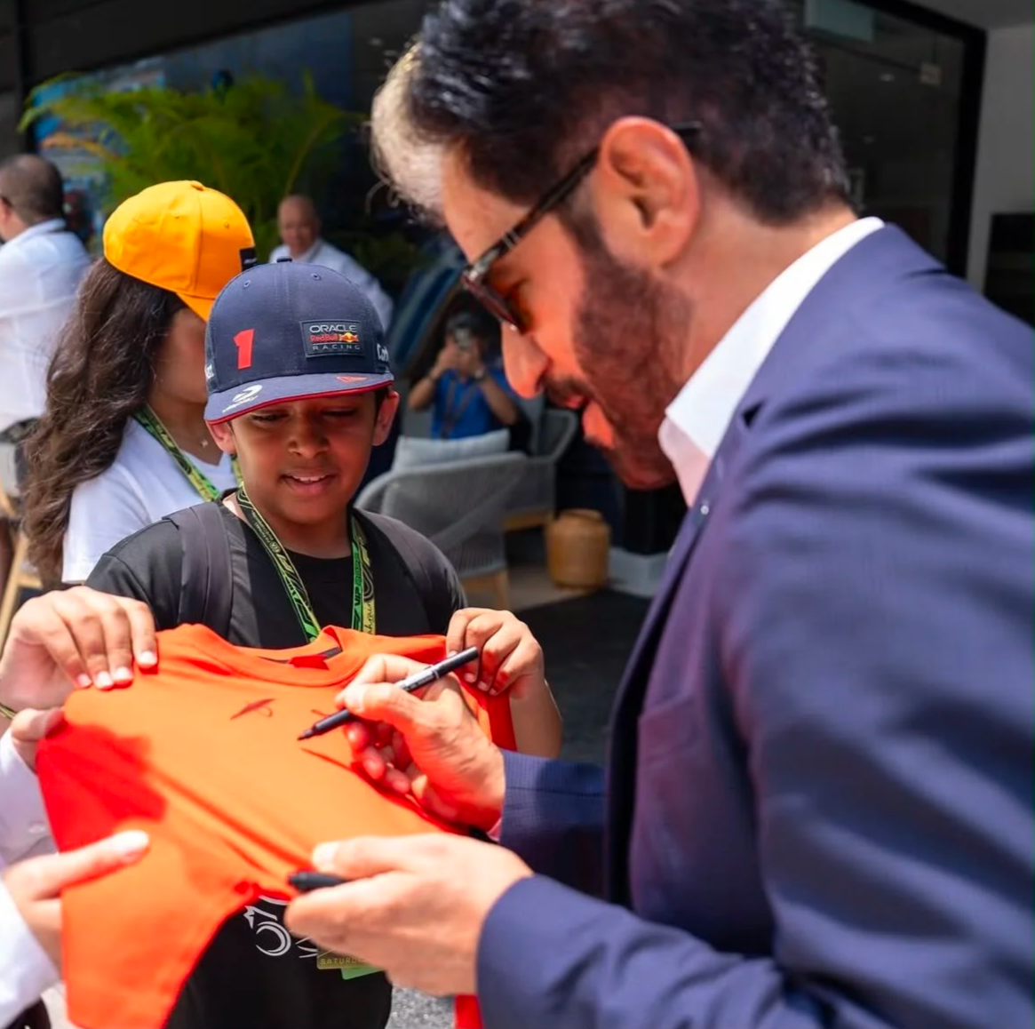 FIA President Mohammed Ben Sulayem signing an orange shirt for a young motorsport fan.
