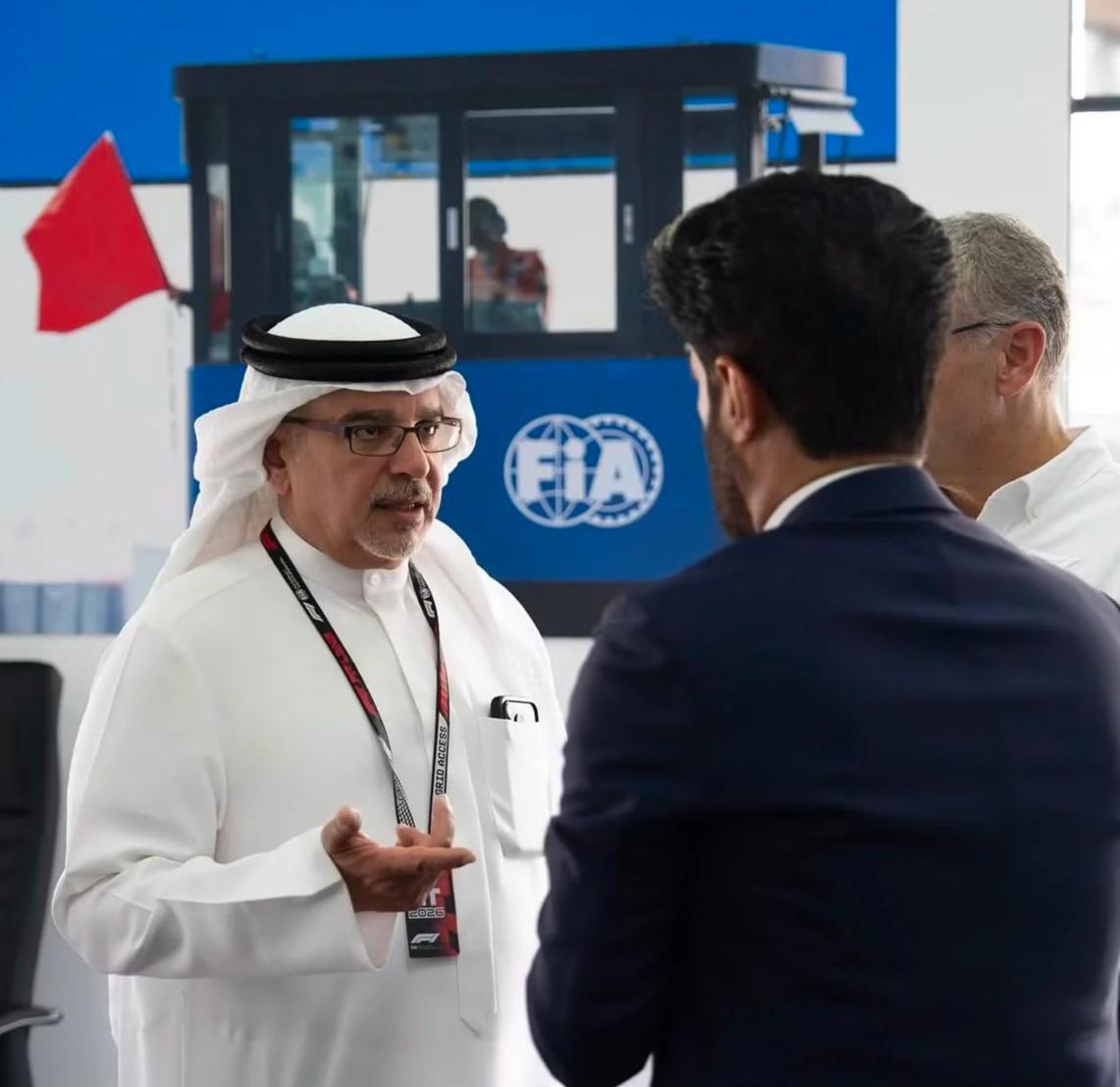 A man in traditional Gulf attire speaking with Mohammed Ben Sulayem beside an FIA trackside station and red flag.