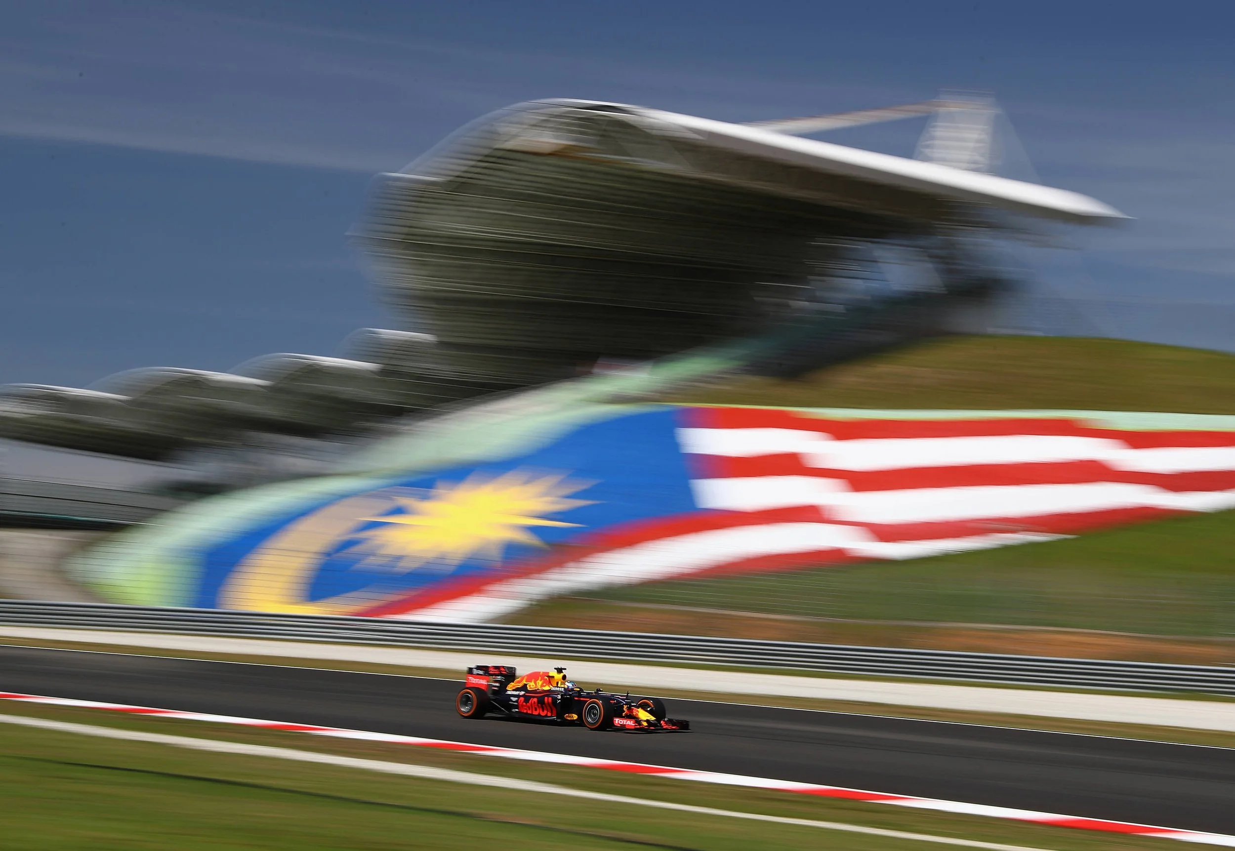Daniel Ricciardo driving his Red Bull past a large Malaysian flag at Sepang International Circuit in 2016.
