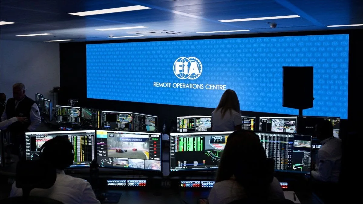Analysts at workstations in the FIA Remote Operations Centre at Biggin Hill, facing a large screen with the FIA logo