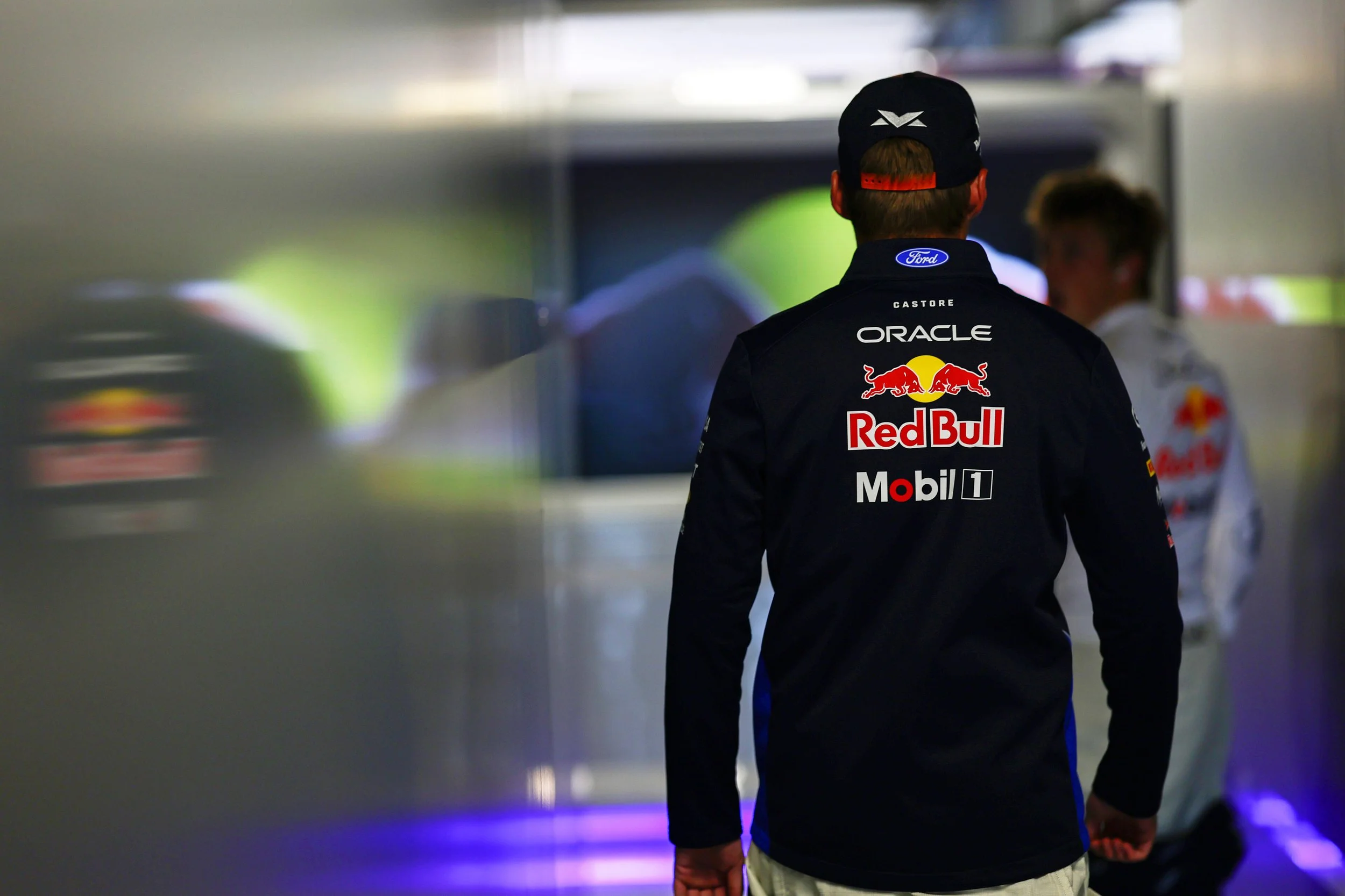 Max Verstappen walks through the Red Bull Racing garage in Red Bull team clothing.