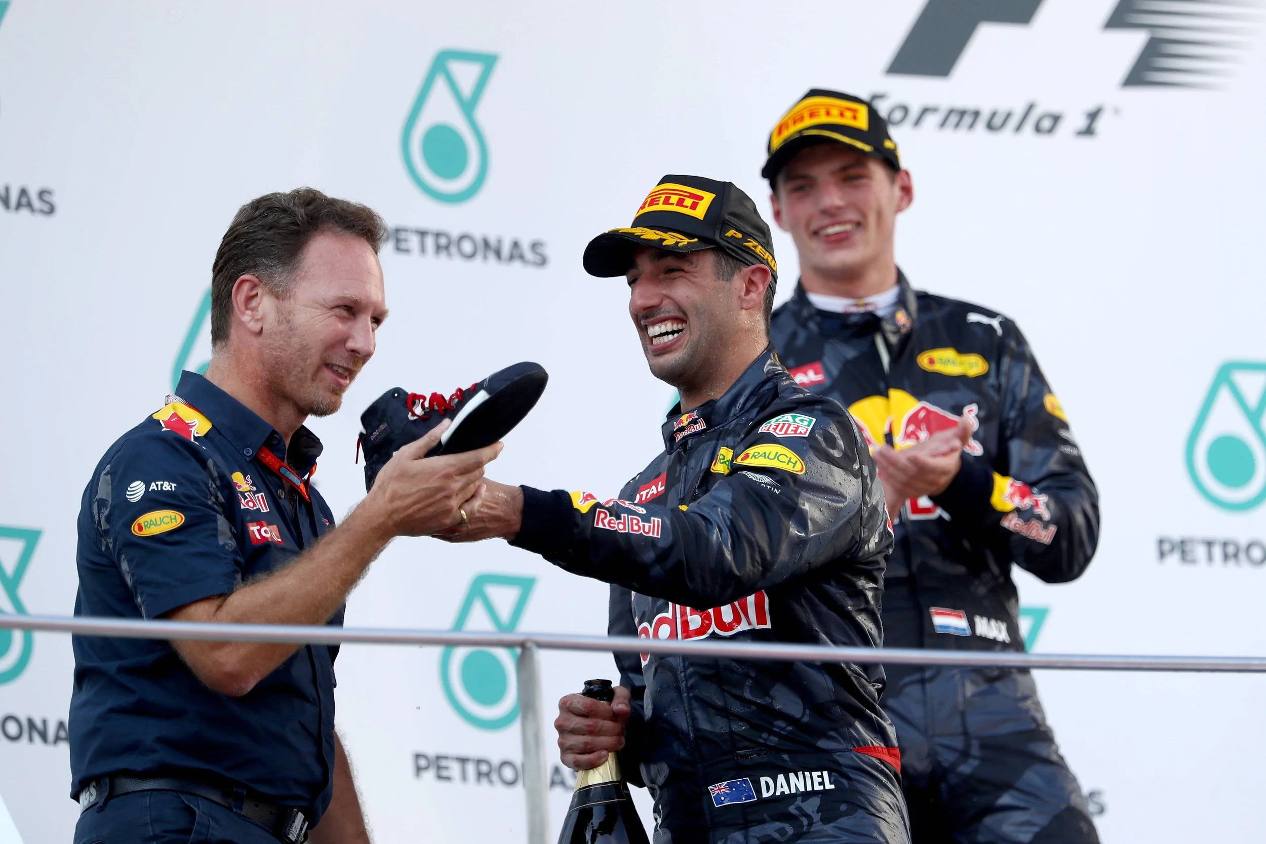 Daniel Ricciardo offering his racing shoe to Christian Horner as Max Verstappen applauds on the 2016 Malaysian Grand Prix podium.