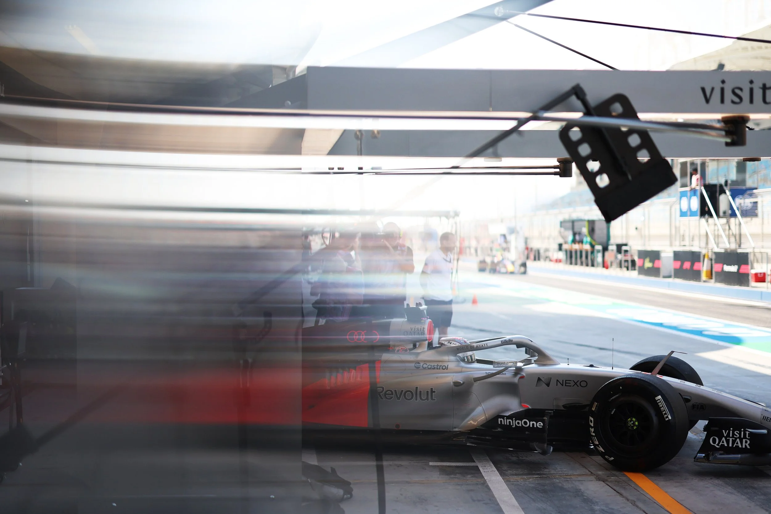 The Cadillac Formula 1 Team in the garage with team members reflected in the glass, with the racing track and pit lane visible outside.