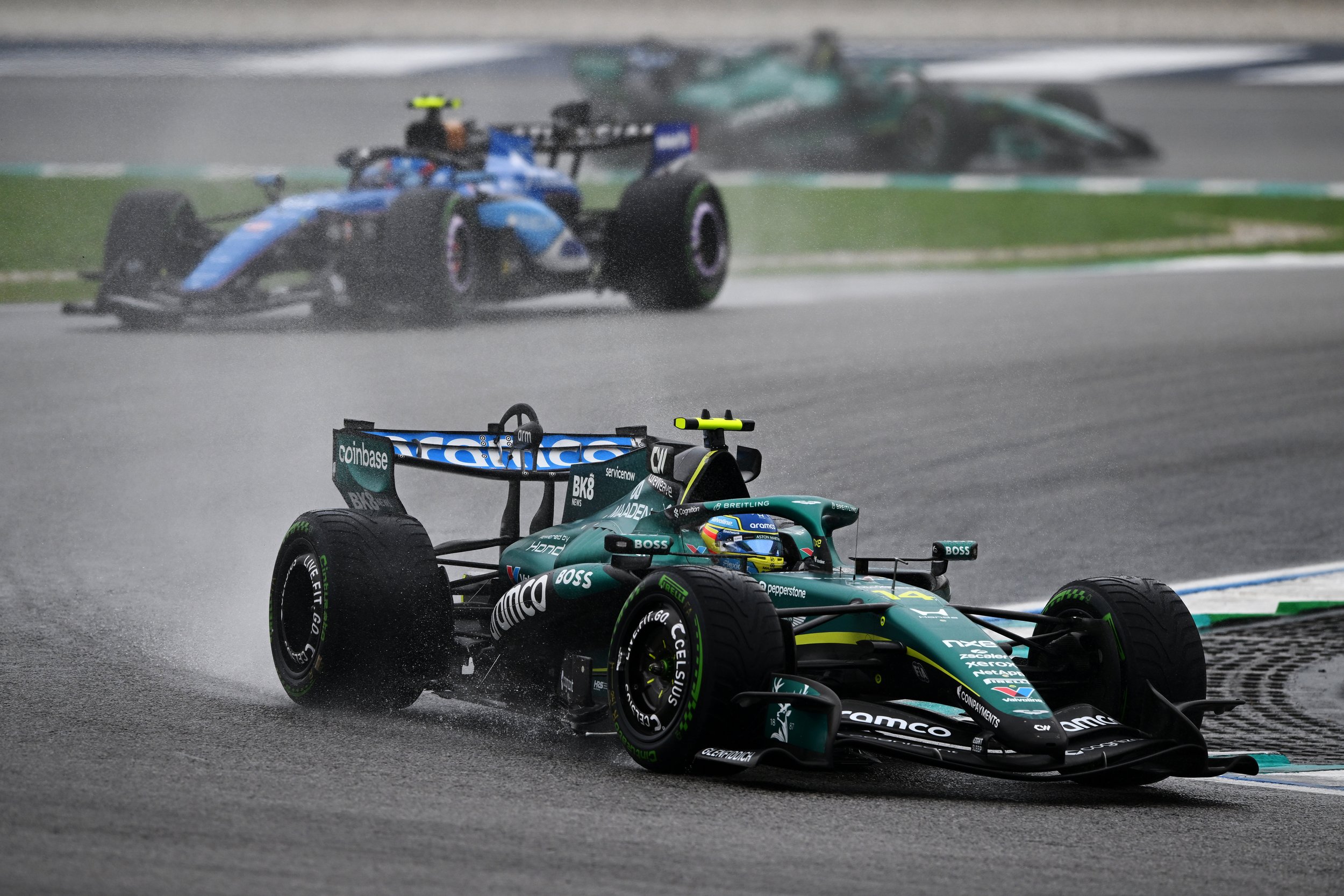 Fernando Alonso driving his Aston Martin through a wet corner at Sepang, with another Formula 1 car following behind.