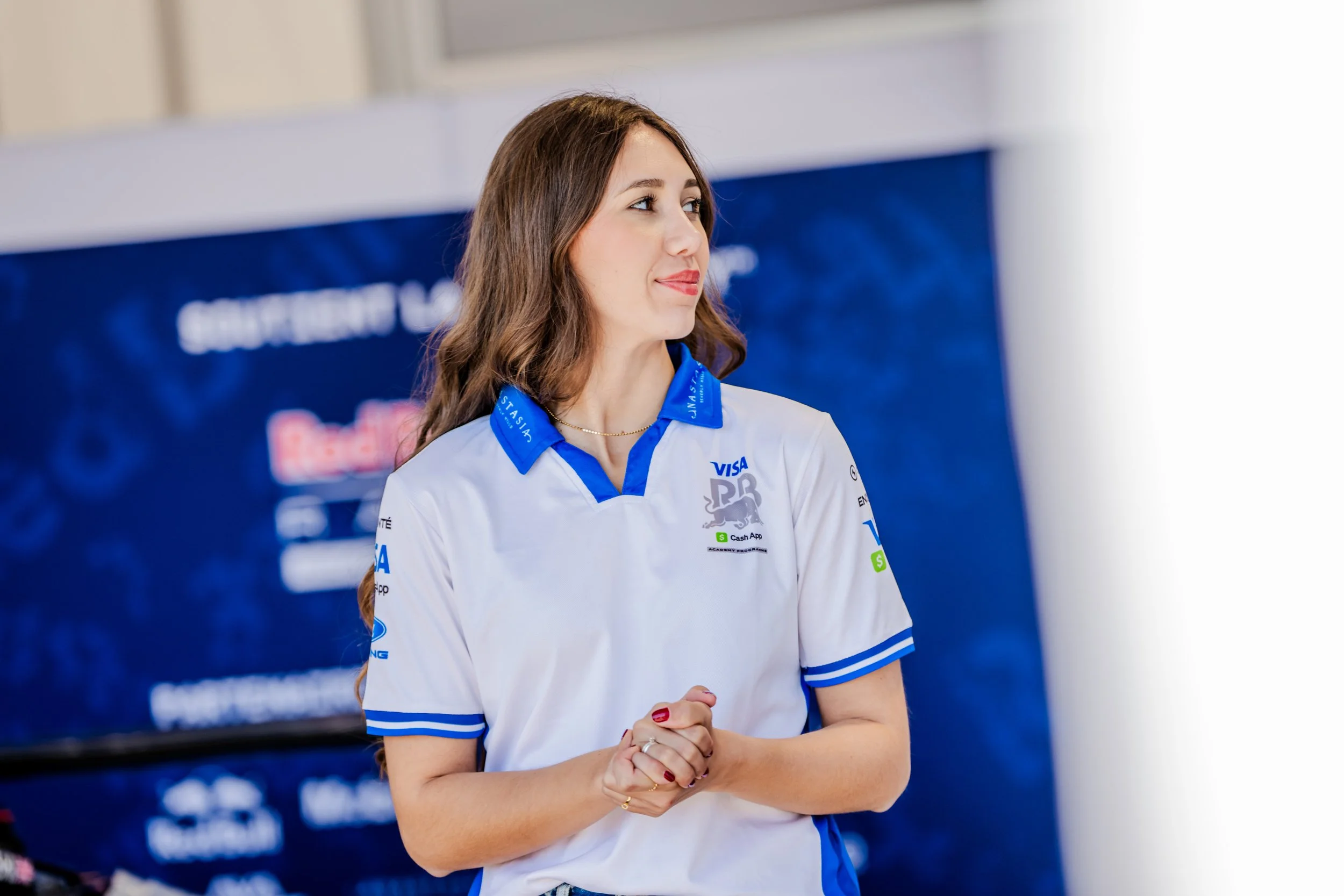 Racing Bulls team member stands in front of a team backdrop during a Formula 1 event.