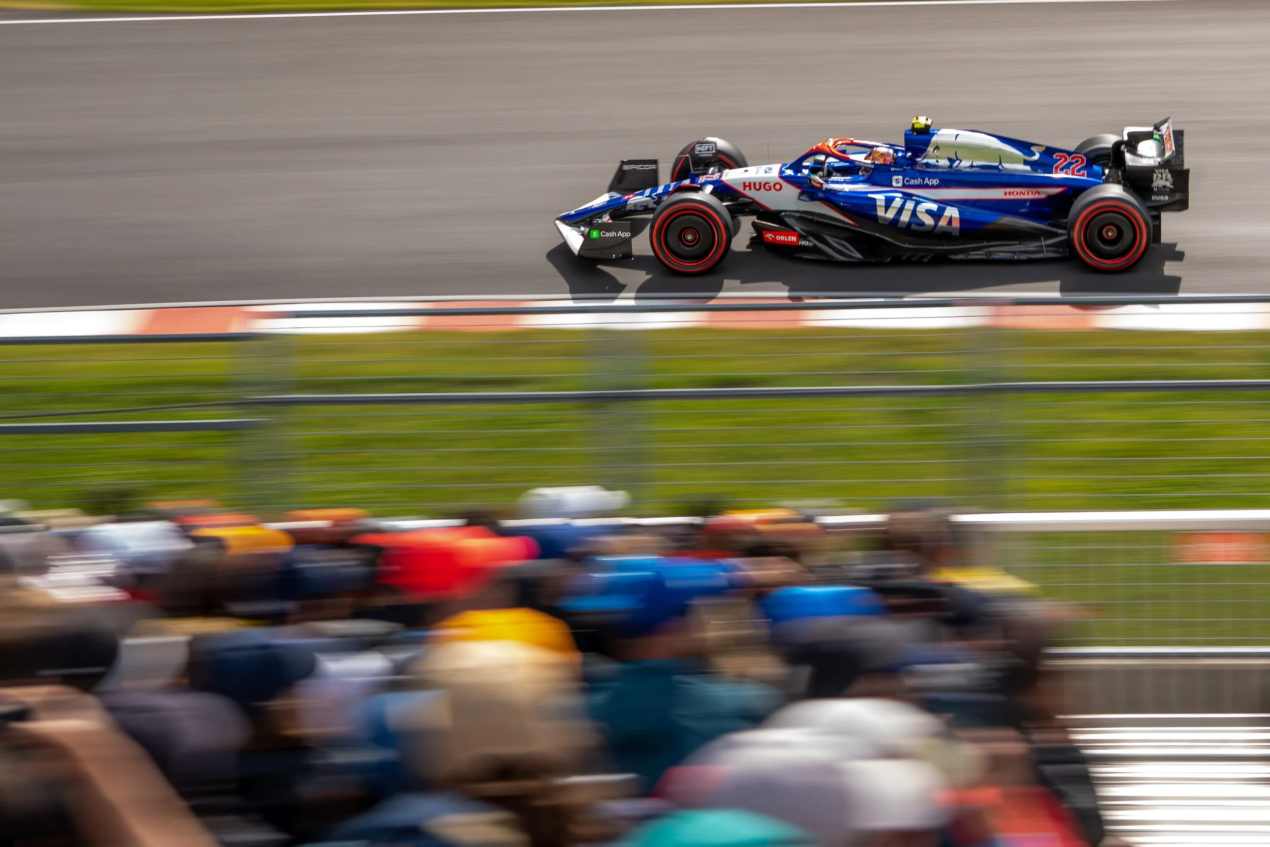 A blue and black Formula 1 car racing on a track with a group of spectators watching from the stands.