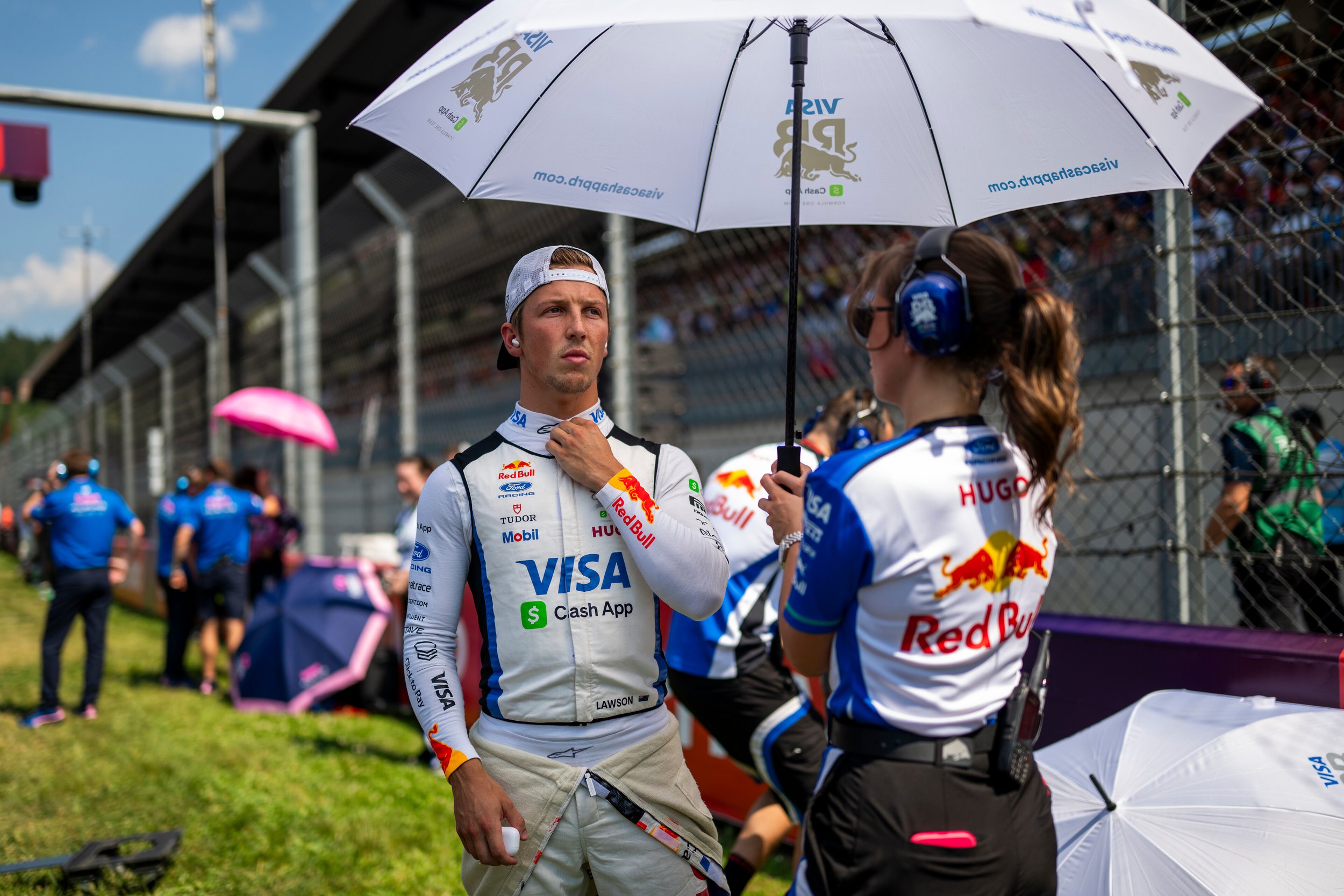 Racing Bulls Formula 1 driver prepares on the grid under a team umbrella during a race weekend.