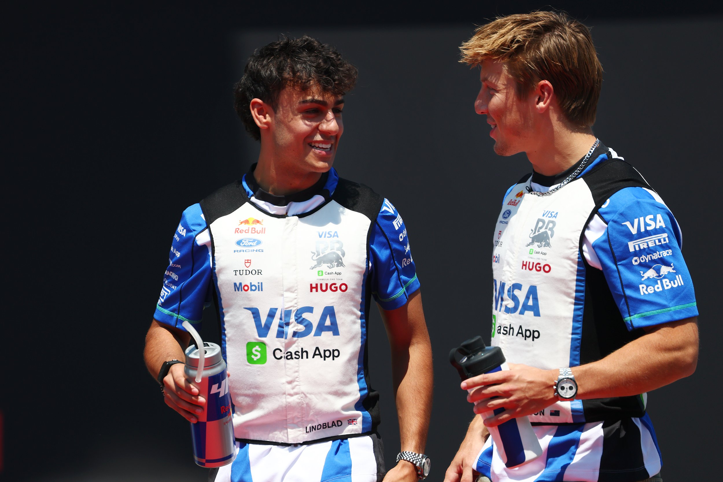Two Racing Bulls Formula 1 drivers talk in team shirts during a race weekend.