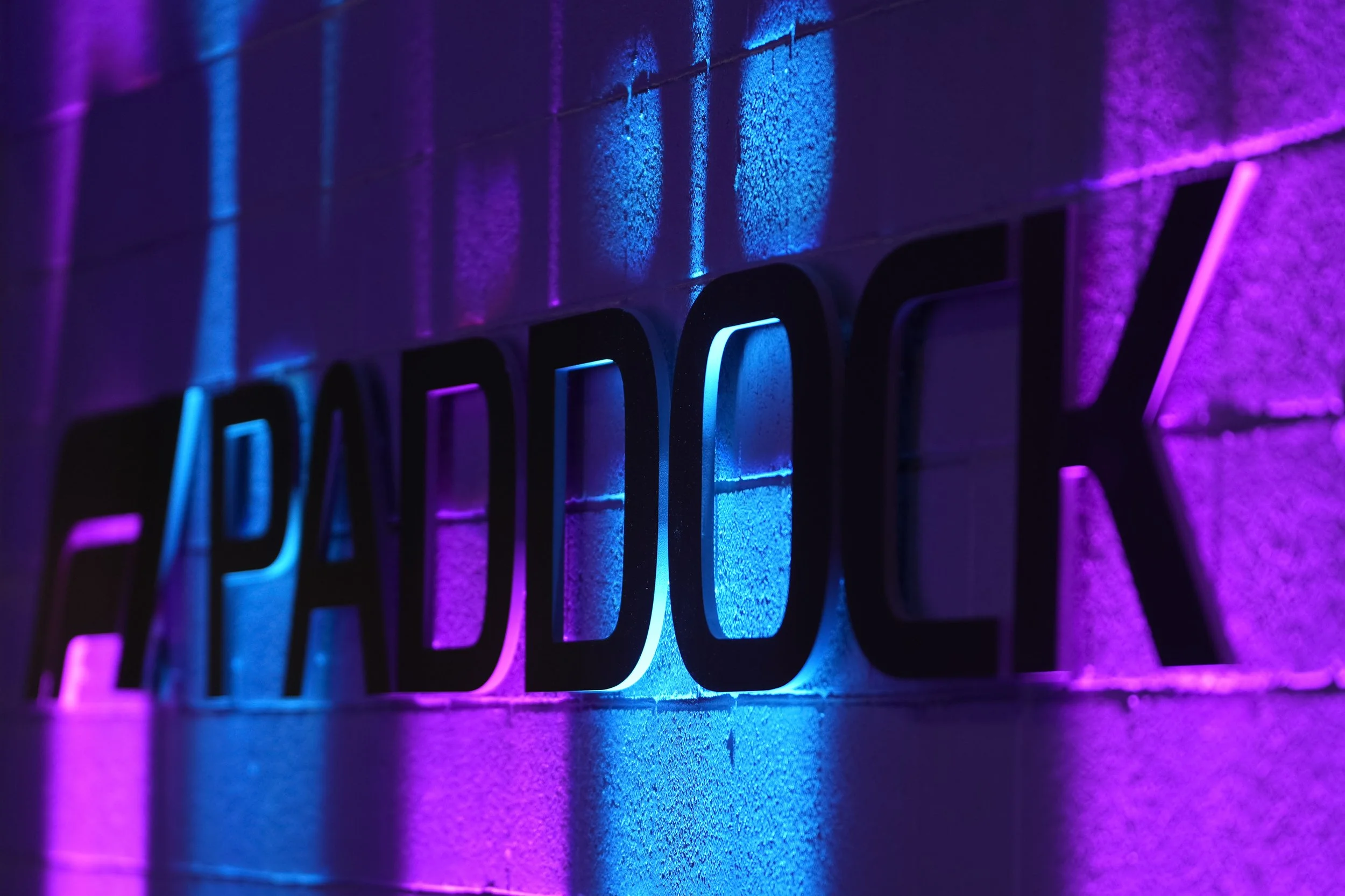 Neon sign with illuminated purple and blue lights on a textured wall.