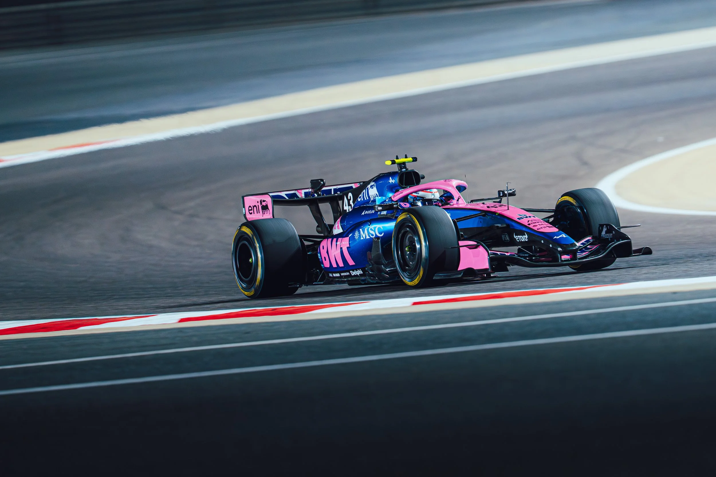 A BWT Alpine Formula One car in blue and pink livery drives through a corner on a race track.