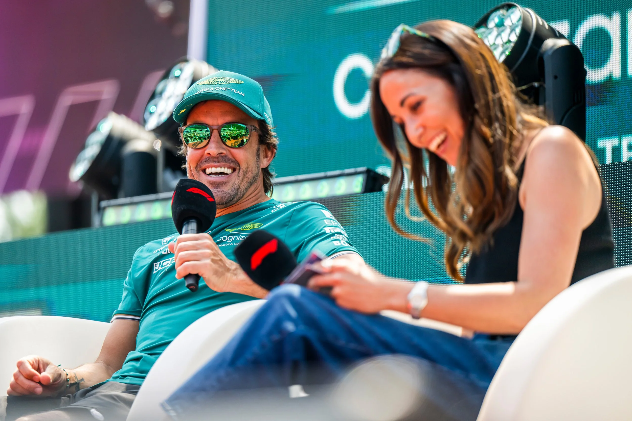 Fernando Alonso smiling during an onstage interview in Aston Martin team clothing