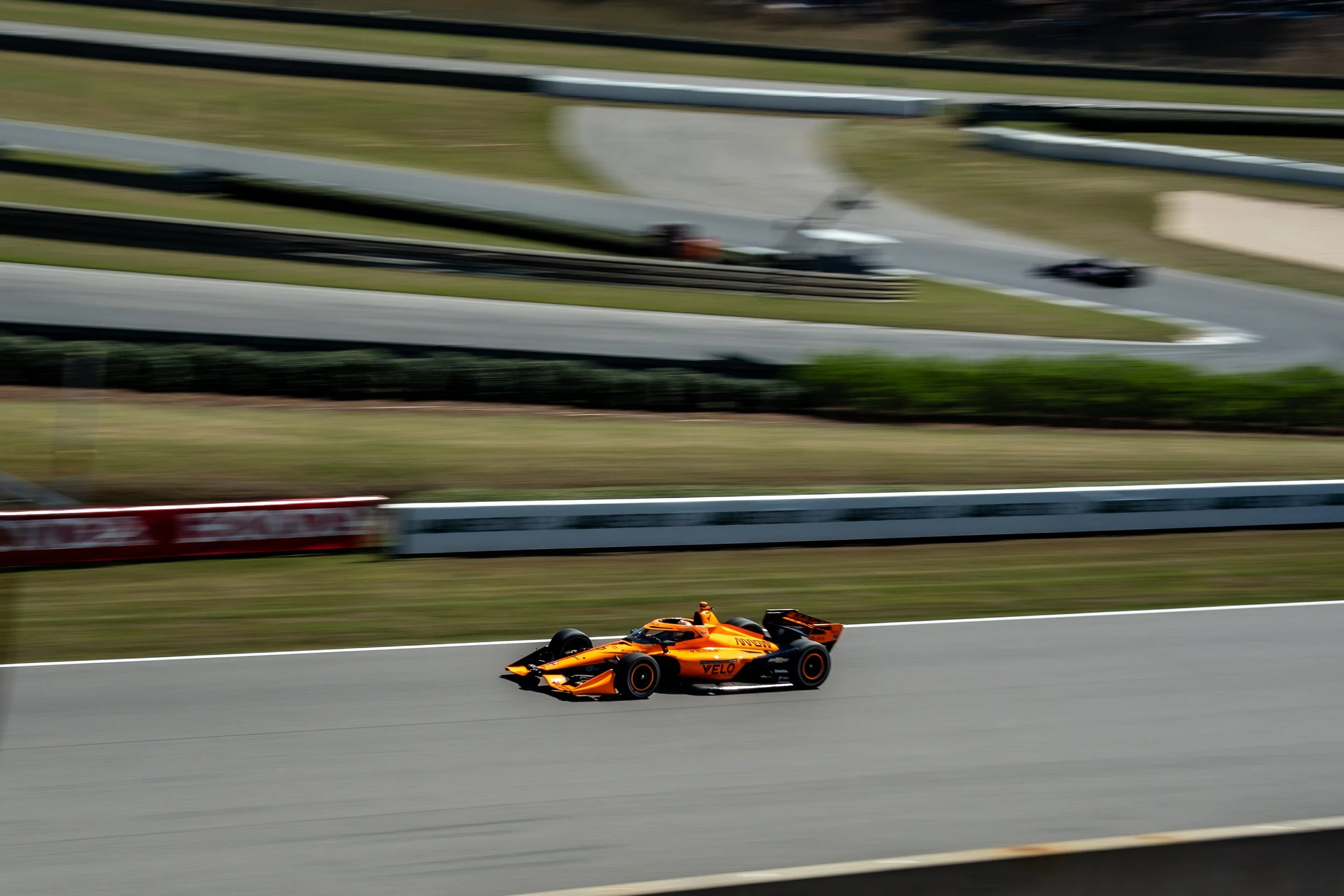 A race car on a race track with blurred background and a grandstand in the distance.