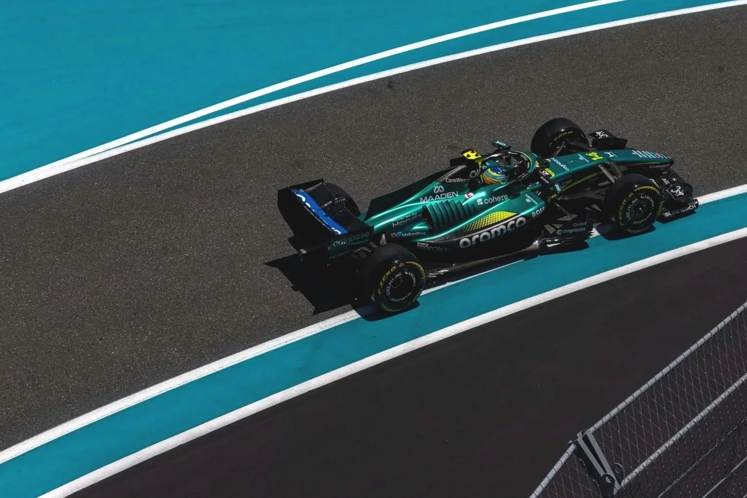 A teal and black Formula 1 car on a racetrack, with a driver in a helmet.