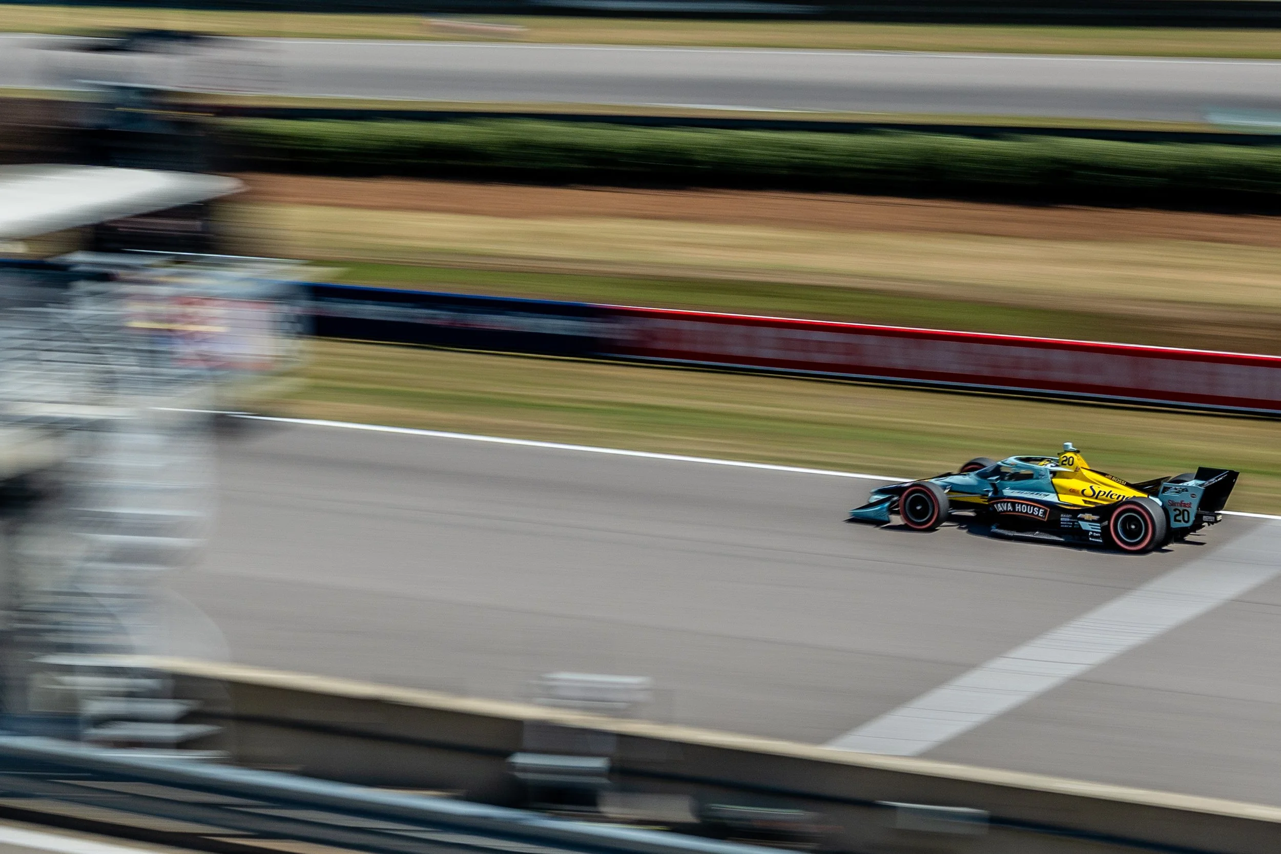 A yellow and black IndyCar racing car speeding on a race track with blurred background indicating high speed.