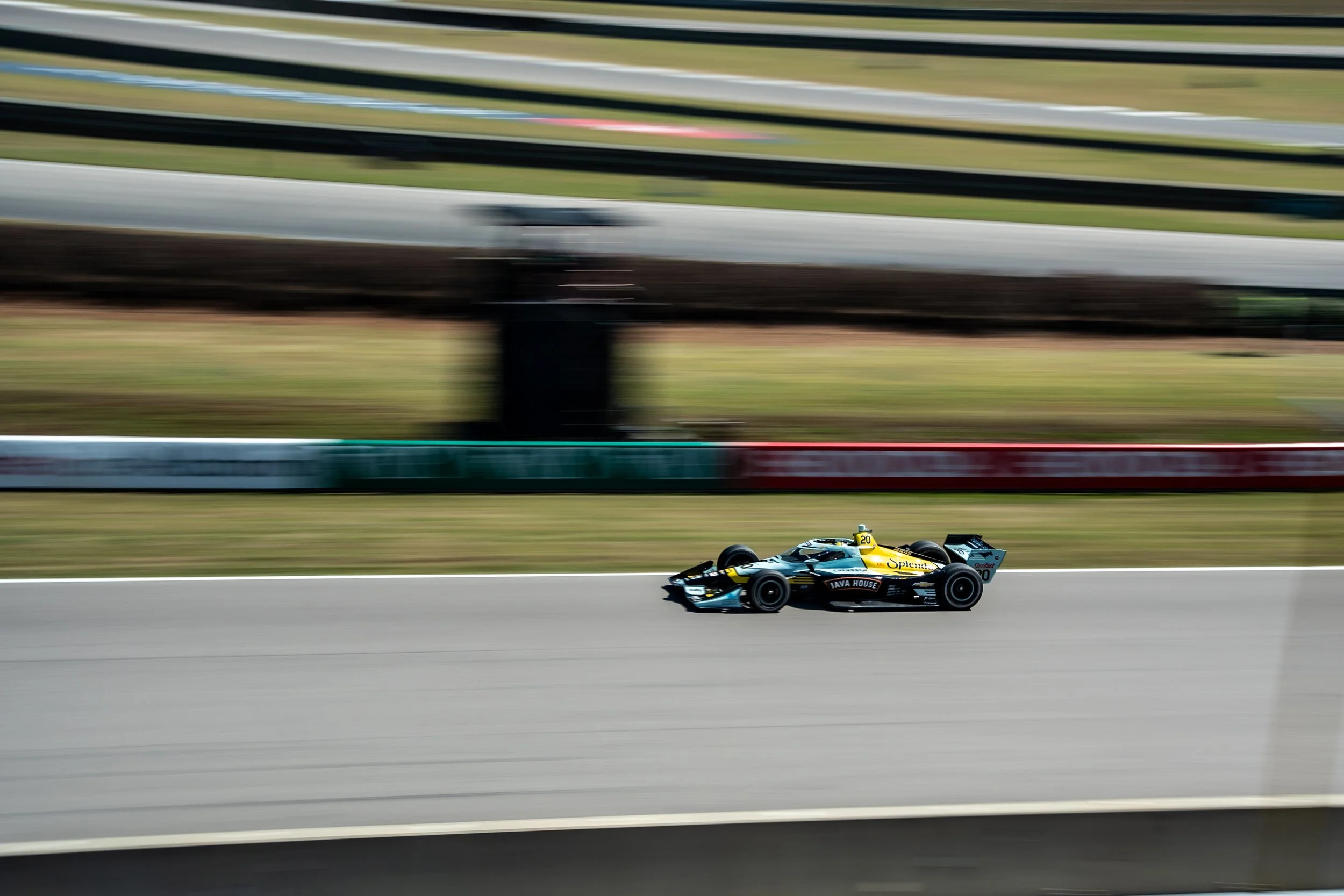 A racing car with a yellow and black color scheme speeding on a race track, with motion blur in the background.