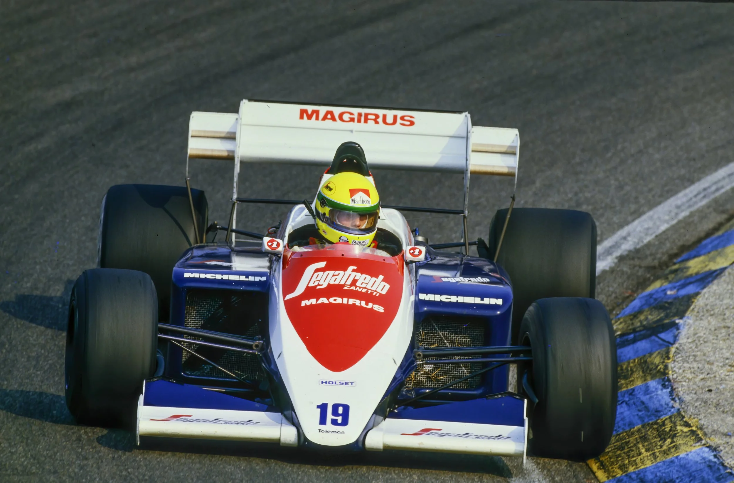 A historic Senna's Formula 1 car with red, white and blue livery races on track during a Grand Prix weekend.