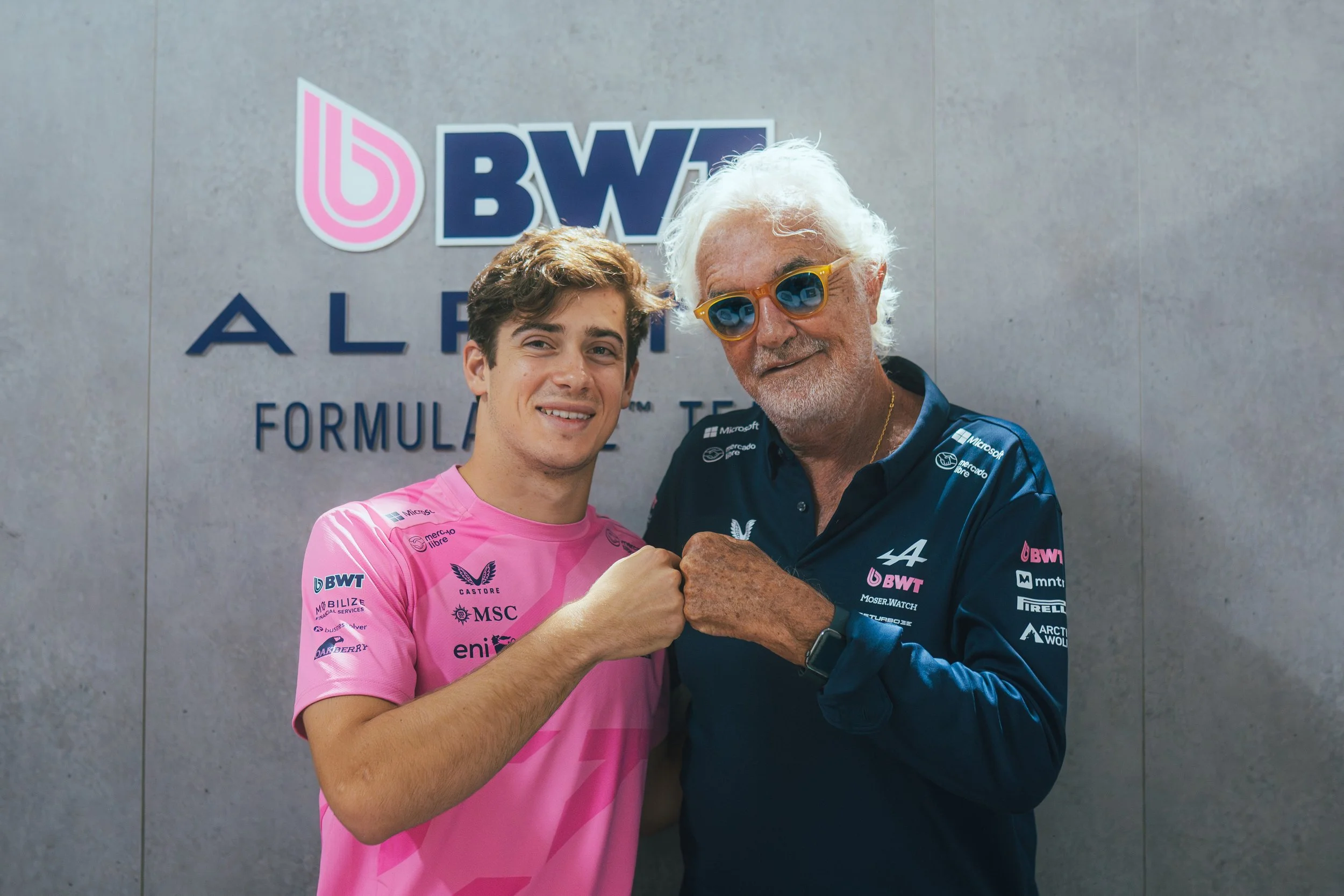 Franco Colapinto and Flavio Briatore pose together in front of the BWT Alpine Formula One Team wall.