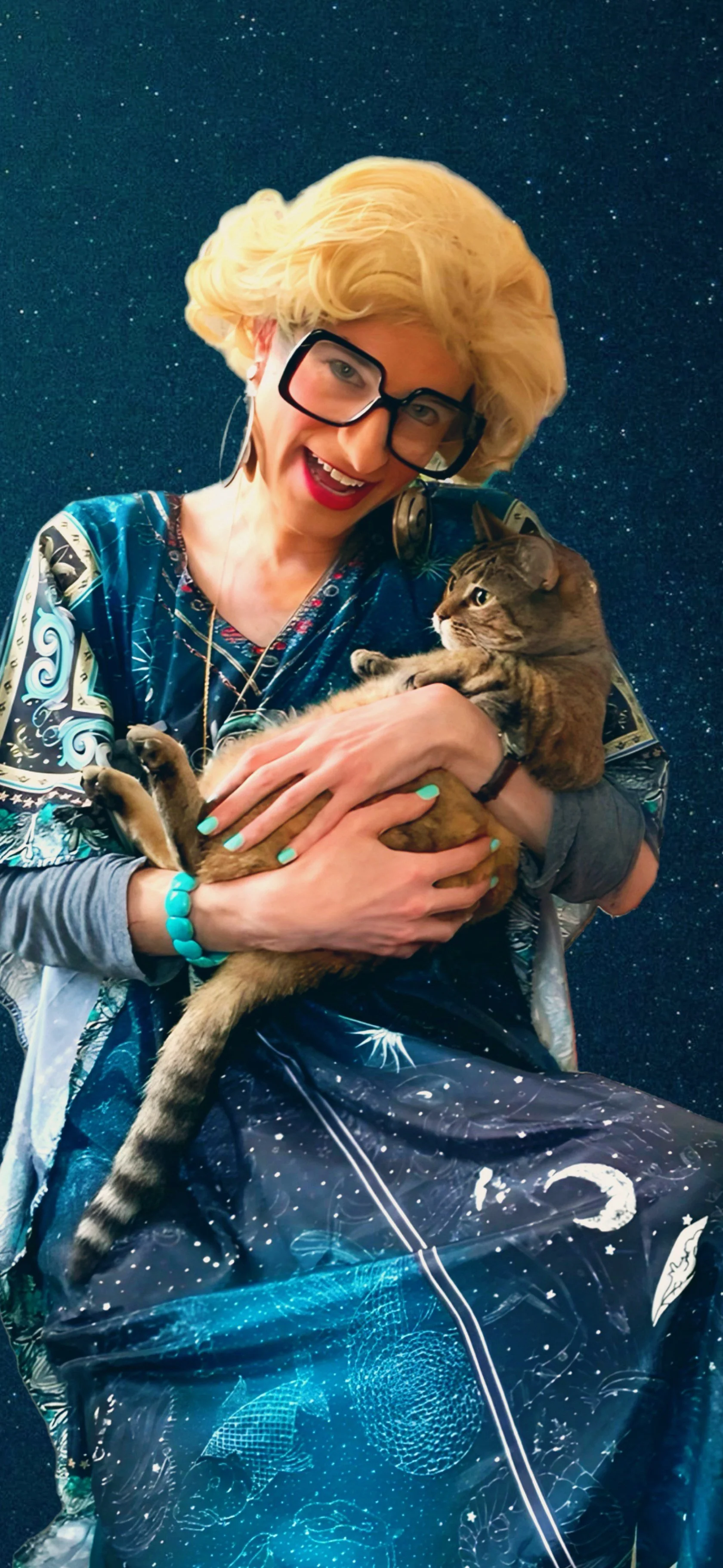 A woman with blonde hair, glasses, red lipstick, wearing a colorful space-themed dress, holding a tabby cat against a starry night background.