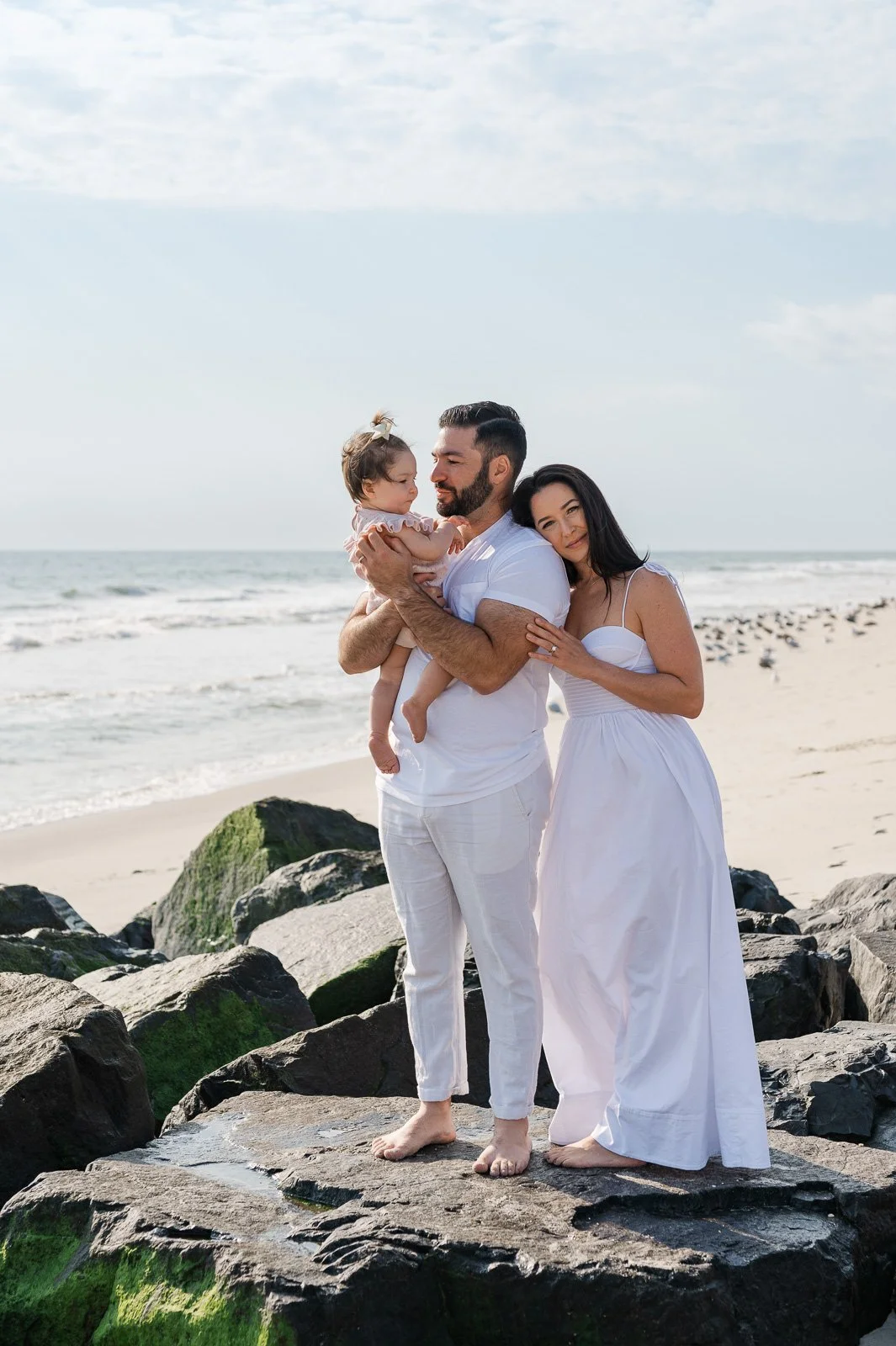 A family at the beach. All are dressed in white, with the ocean and sky in the background. Family photography.
