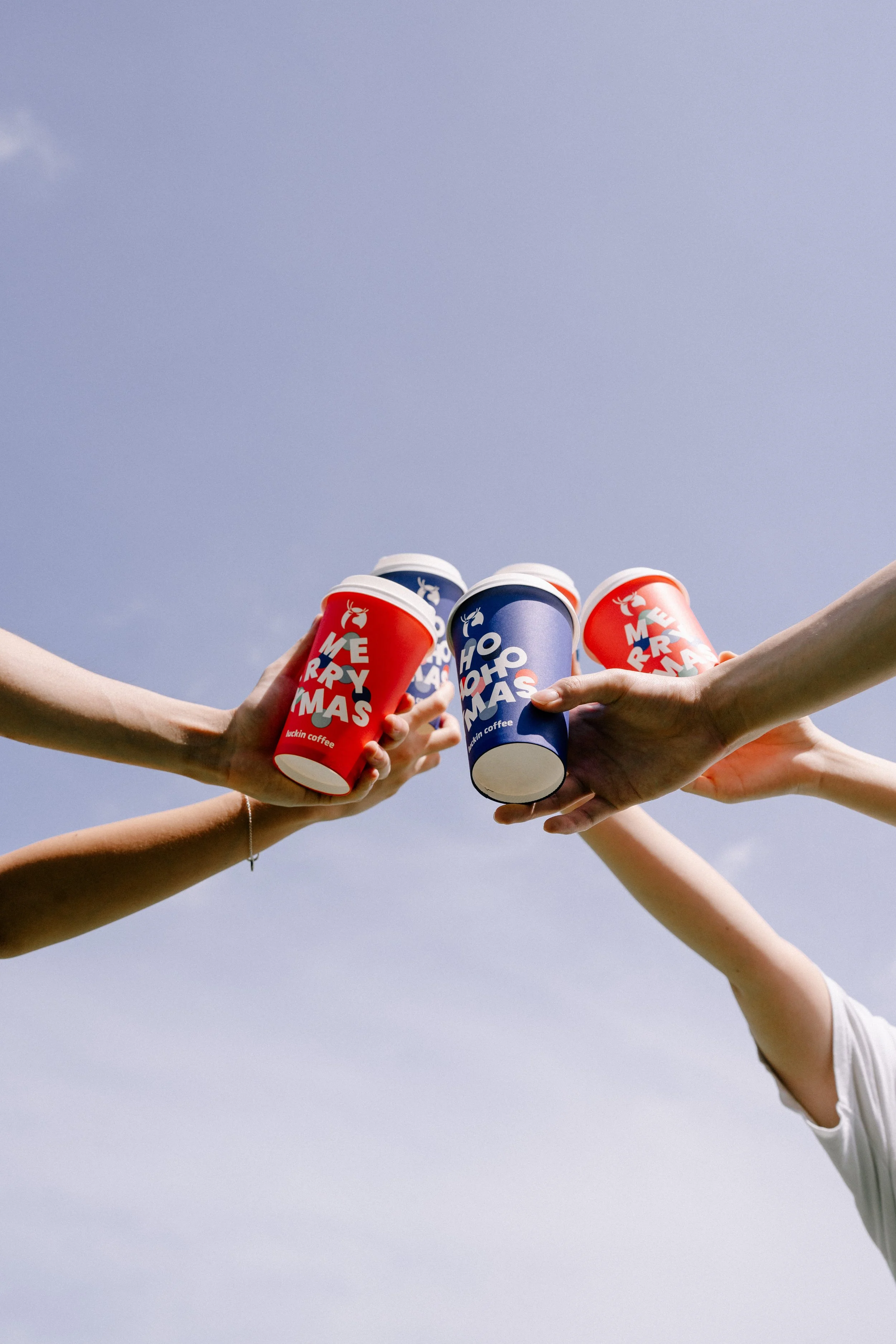 People holding up holiday-themed coffee cups with a clear sky in the background.