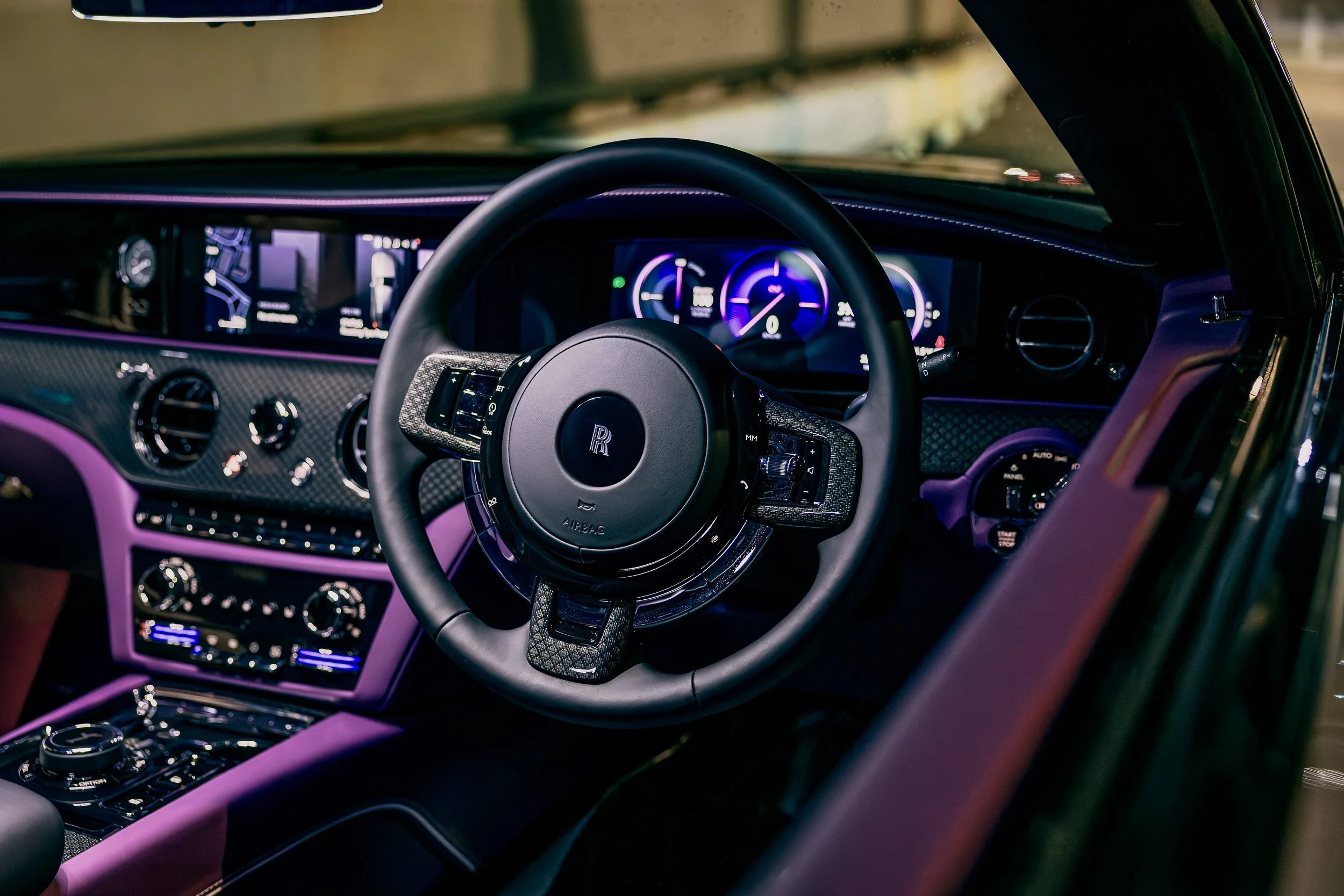 Interior of a luxury car with a leather steering wheel, digital dashboard, and purple interior accents.