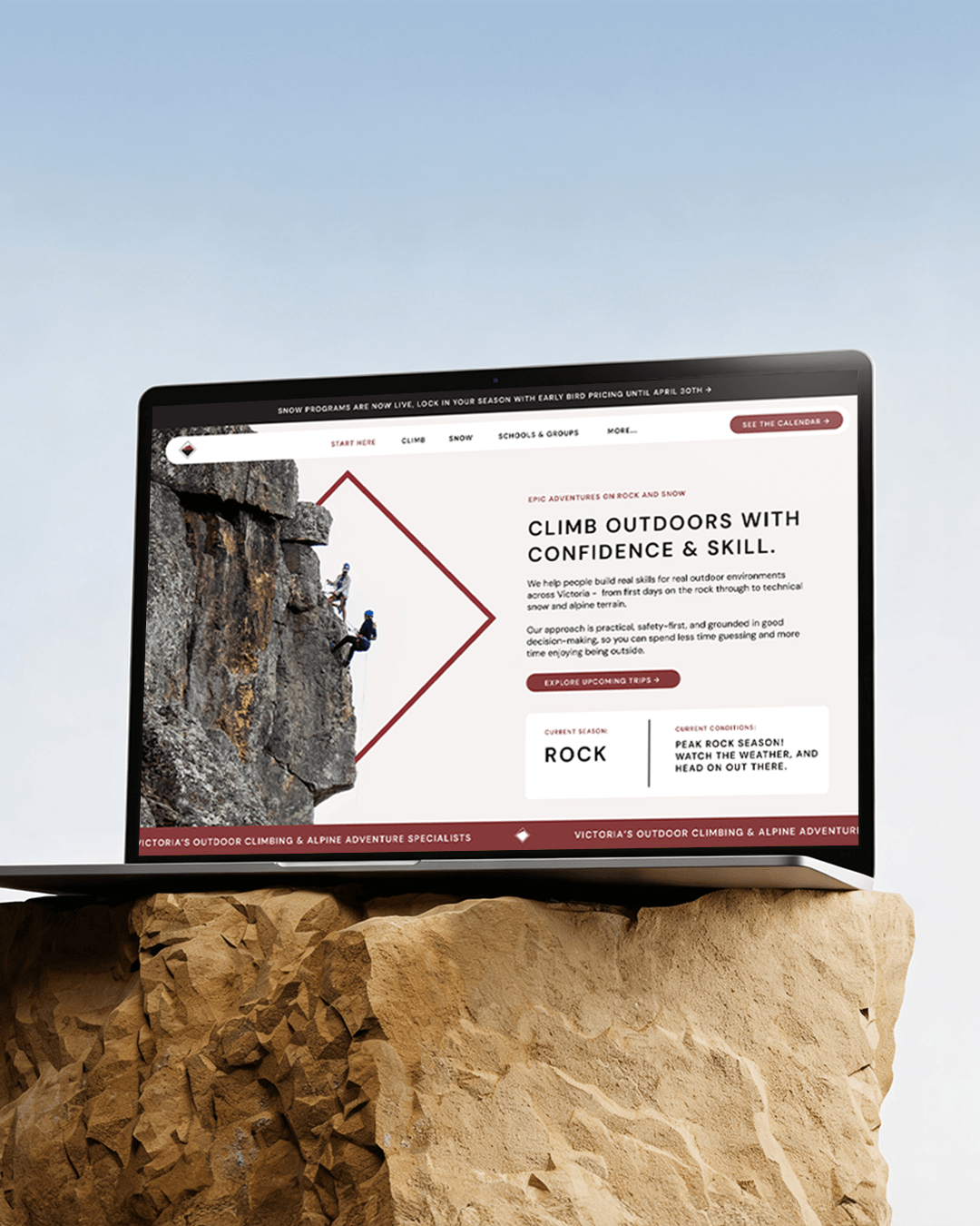 A laptop displaying a website for outdoor climbing and alpine adventure, placed on a large rock against a clear sky.