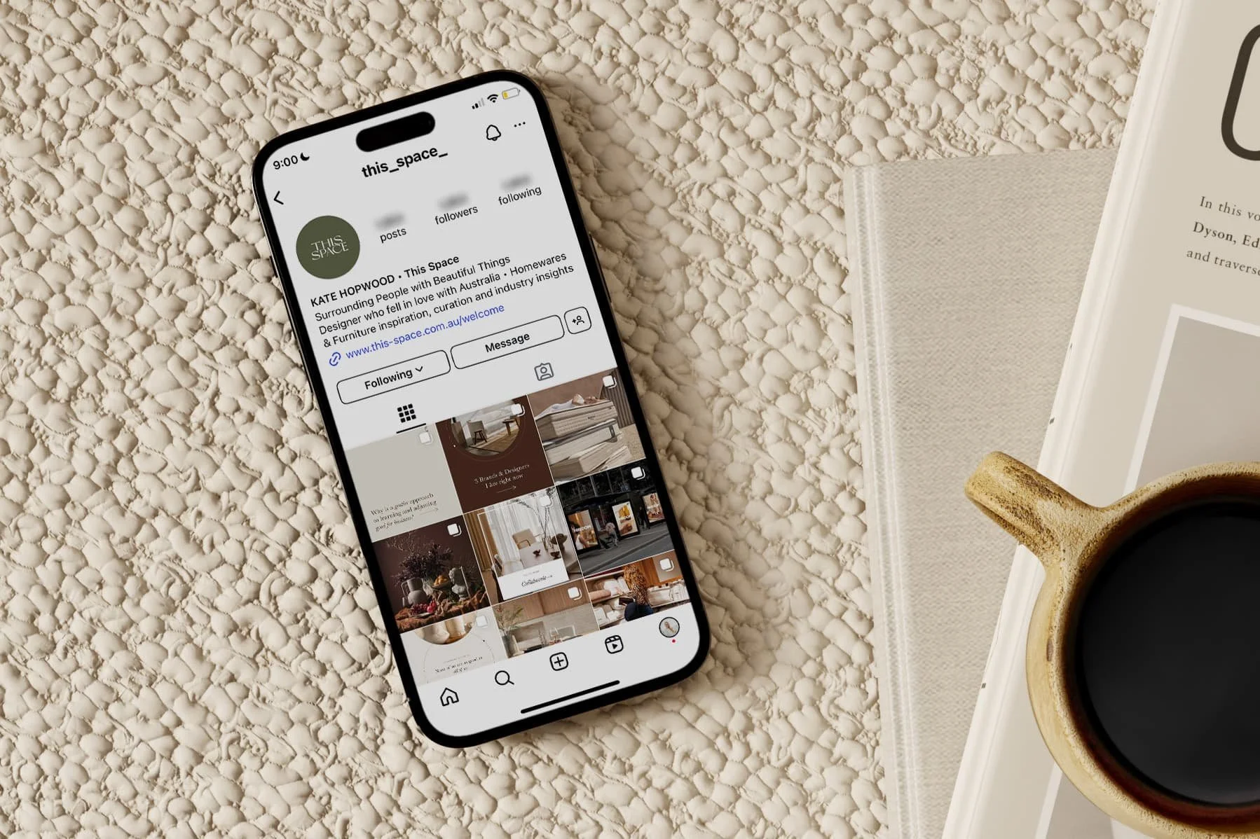 An iPhone displaying an Instagram profile named this_space_ on a textured beige surface, with a book, a napkin, and a cup of black coffee nearby.