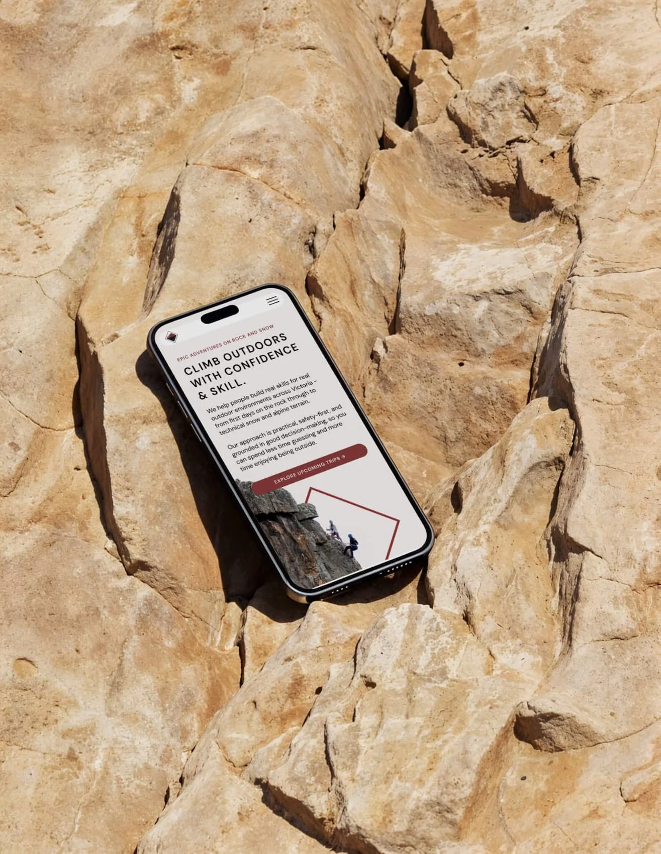 Smartphone resting on large rocks displaying a webpage about outdoor rock climbing adventures.