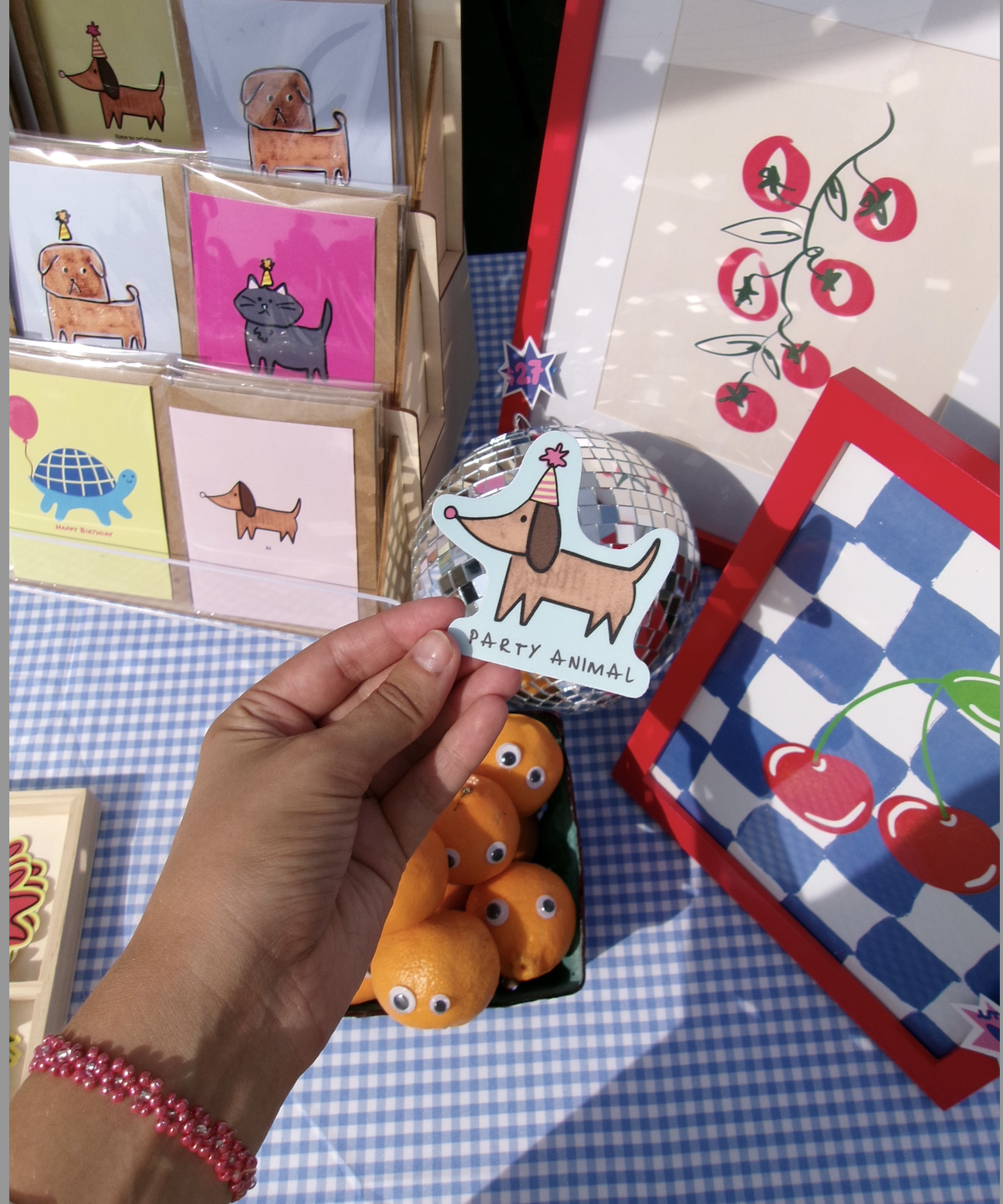 Decorative store display featuring party-themed animal items, including flashcards with illustrated animals and accessories, a wire ball with a dog craft labeled "Party Animal," a basket of oranges with googly eyes, and framed pictures of animals and