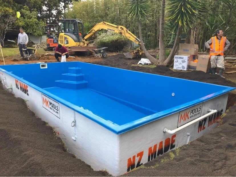 An above-ground swimming pool under construction with workers and construction equipment nearby.