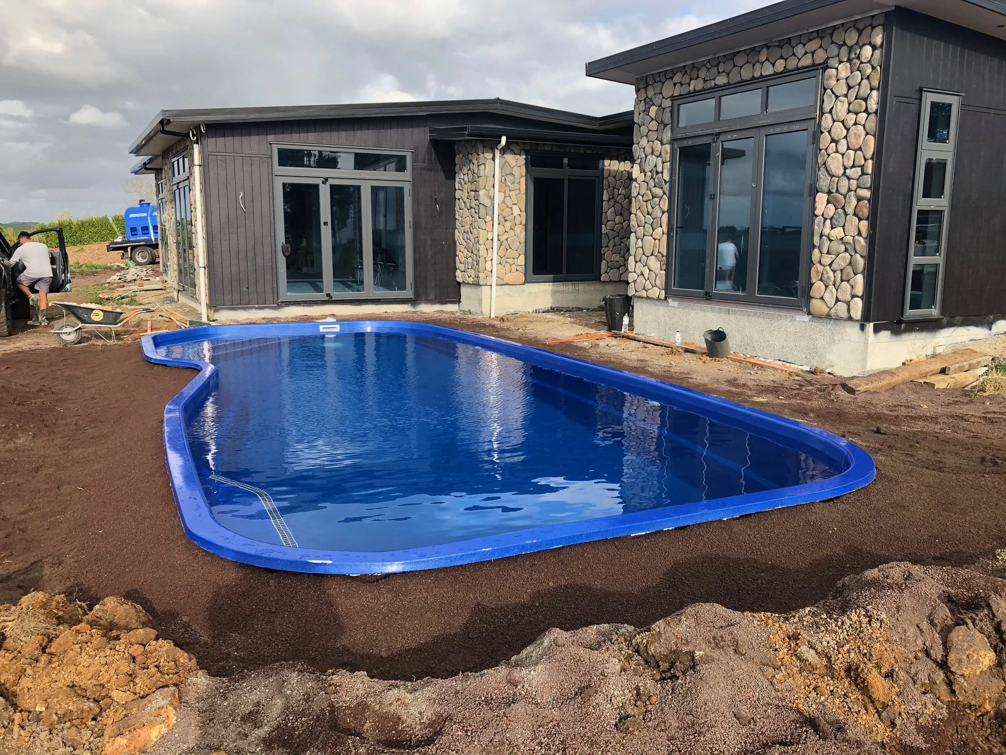 Newly constructed house with large windows and a backyard swimming pool, under cloudy skies.