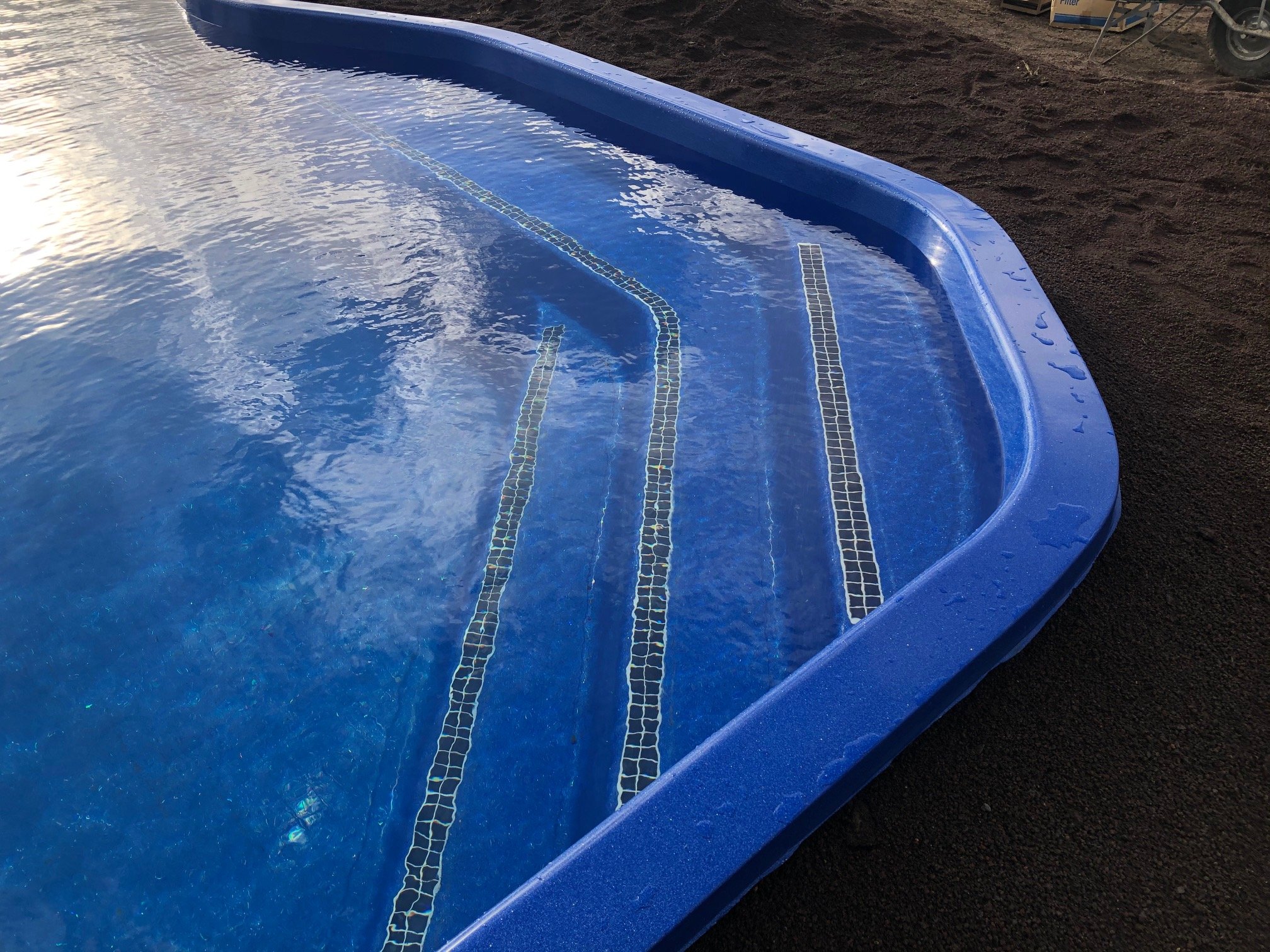 Close-up of an empty outdoor swimming pool with blue tiles along the bottom, with some water reflections and a dark ground surrounding it.