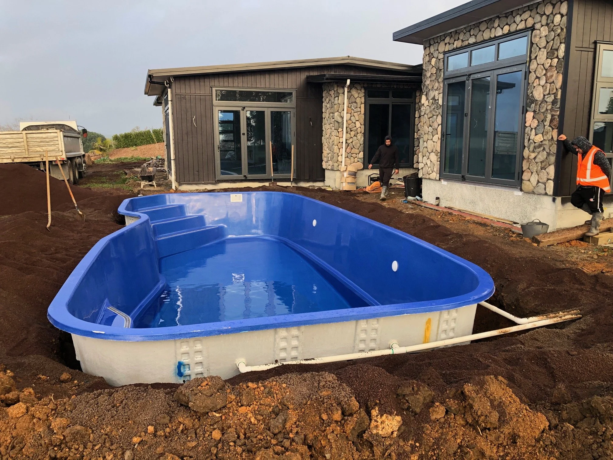 Construction workers installing an in-ground swimming pool in a backyard basketball court under construction.
