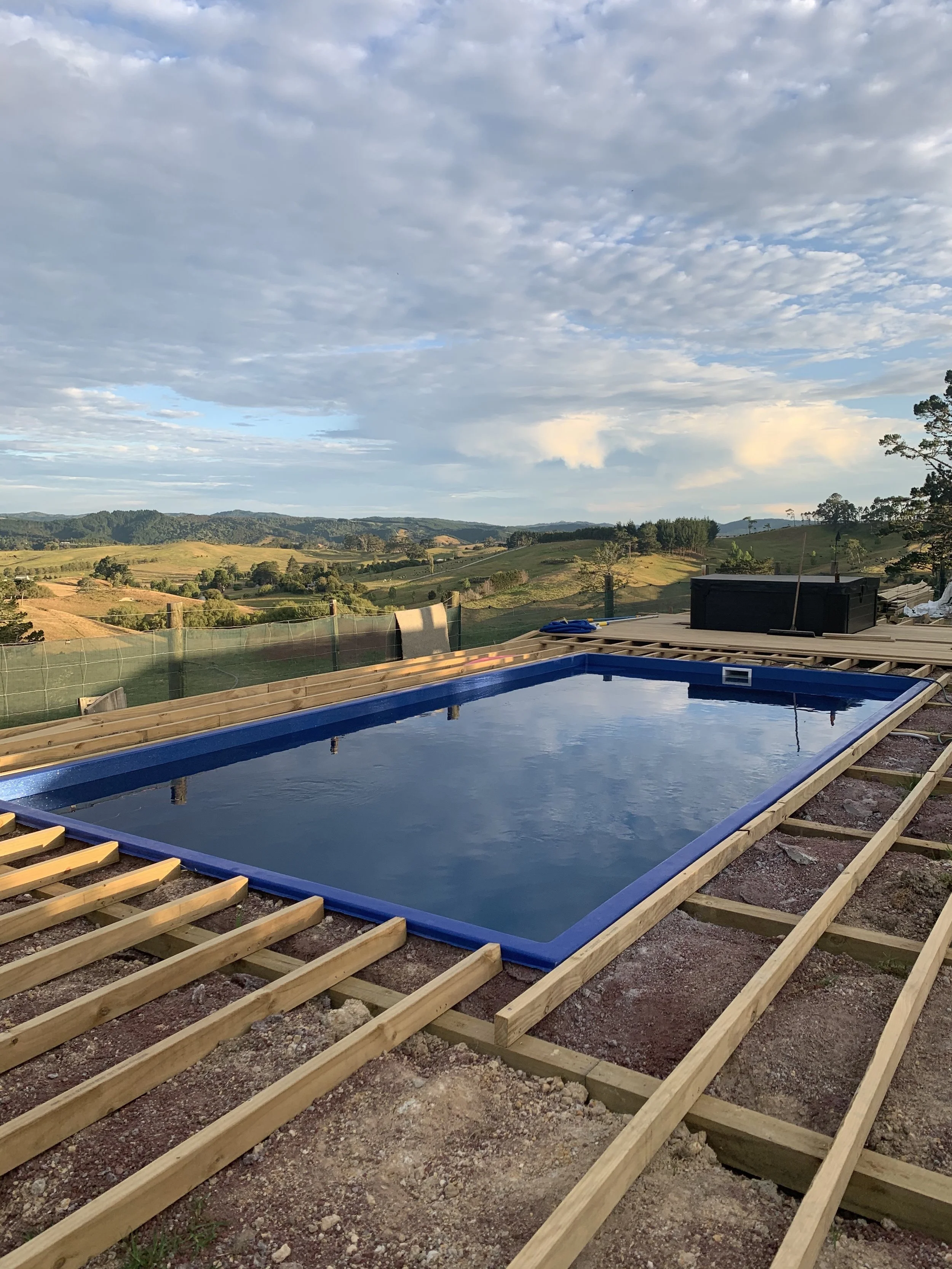 A swimming pool under construction on a hilltop with scenic rolling hills and cloudy sky in the background.