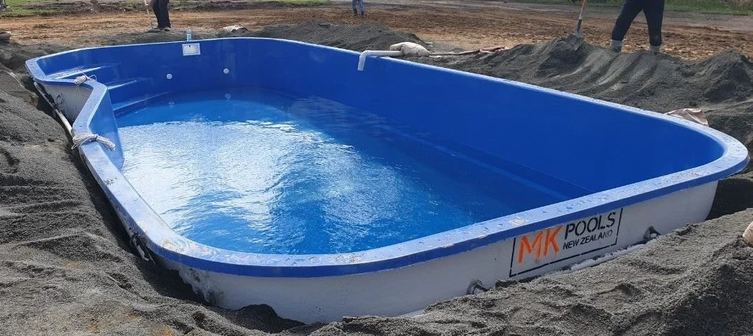 A new above-ground swimming pool partially filled with water, installed in a sandy area with a few people in the background.