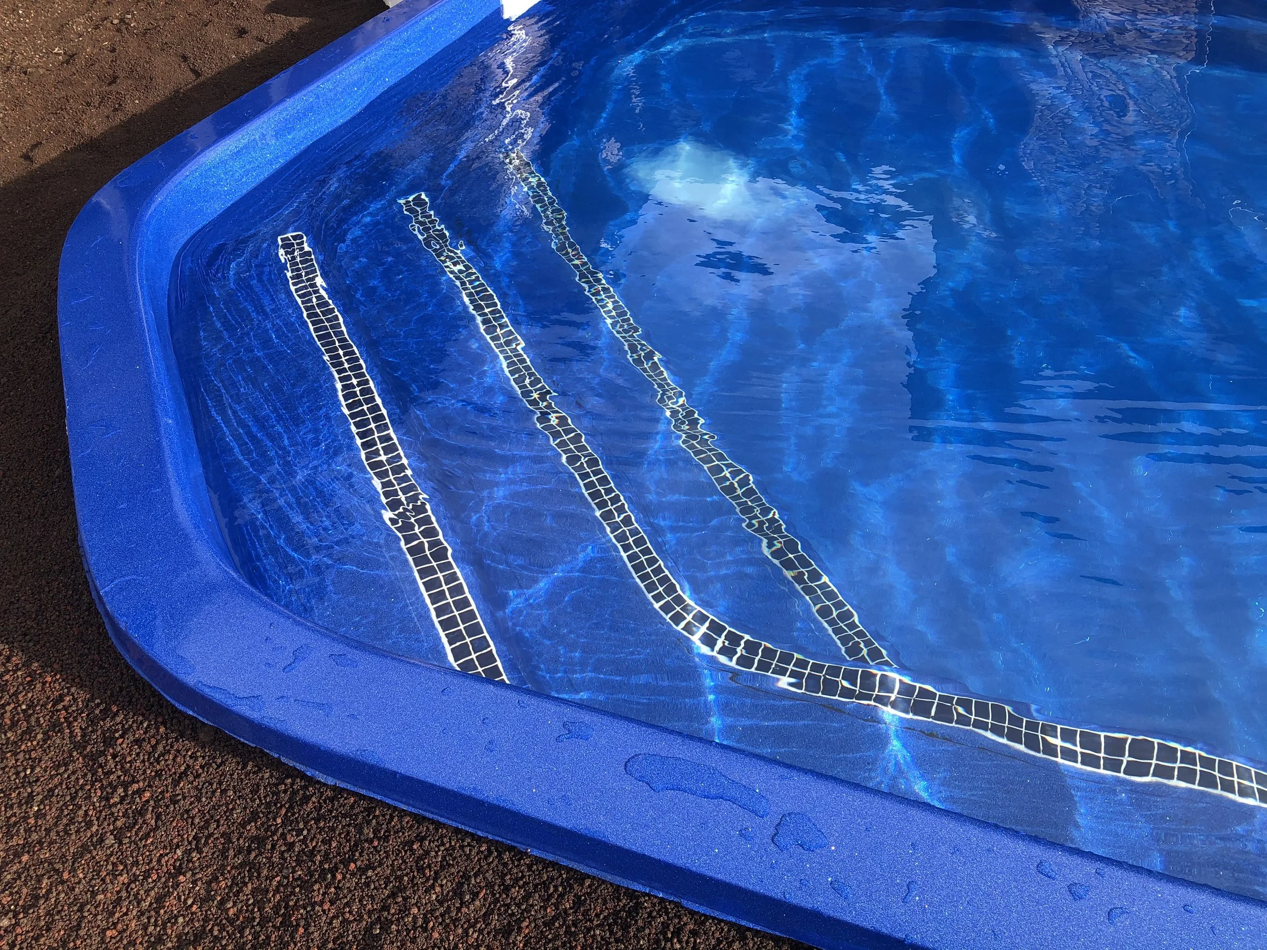 Close-up of the edge and steps of a blue swimming pool with water reflecting the sky.