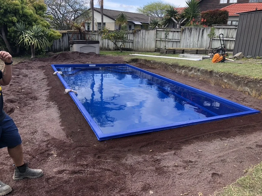 In-ground swimming pool with a blue liner being installed in a backyard, surrounded by dirt and construction materials.