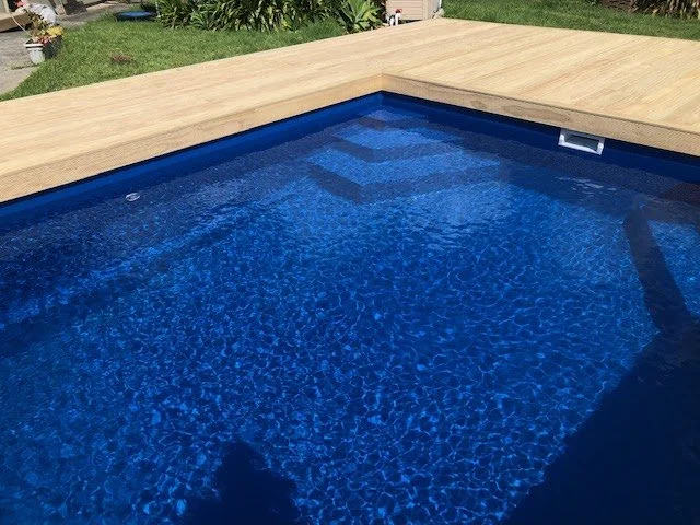 In-ground swimming pool with blue water and a wooden deck.