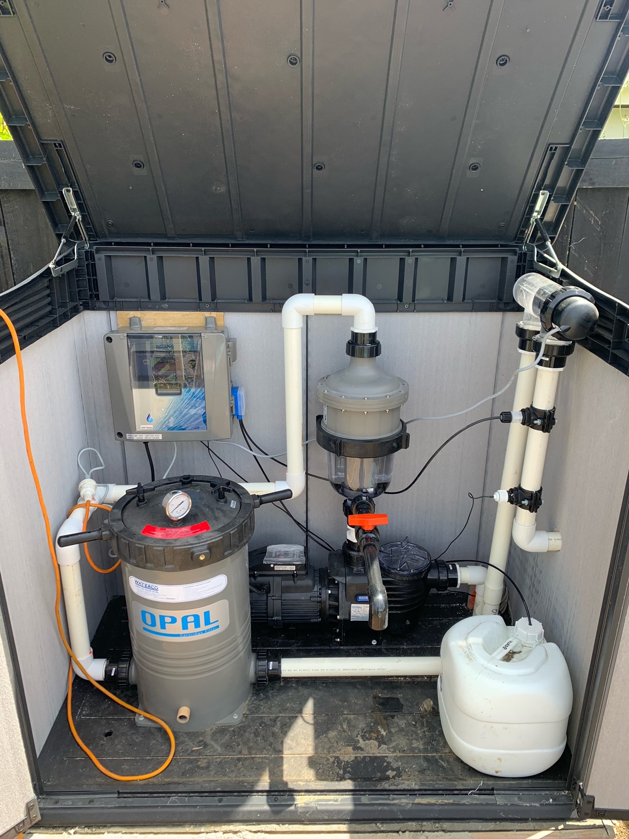 An outdoor pool equipment box containing a filter, pump, and water treatment components.