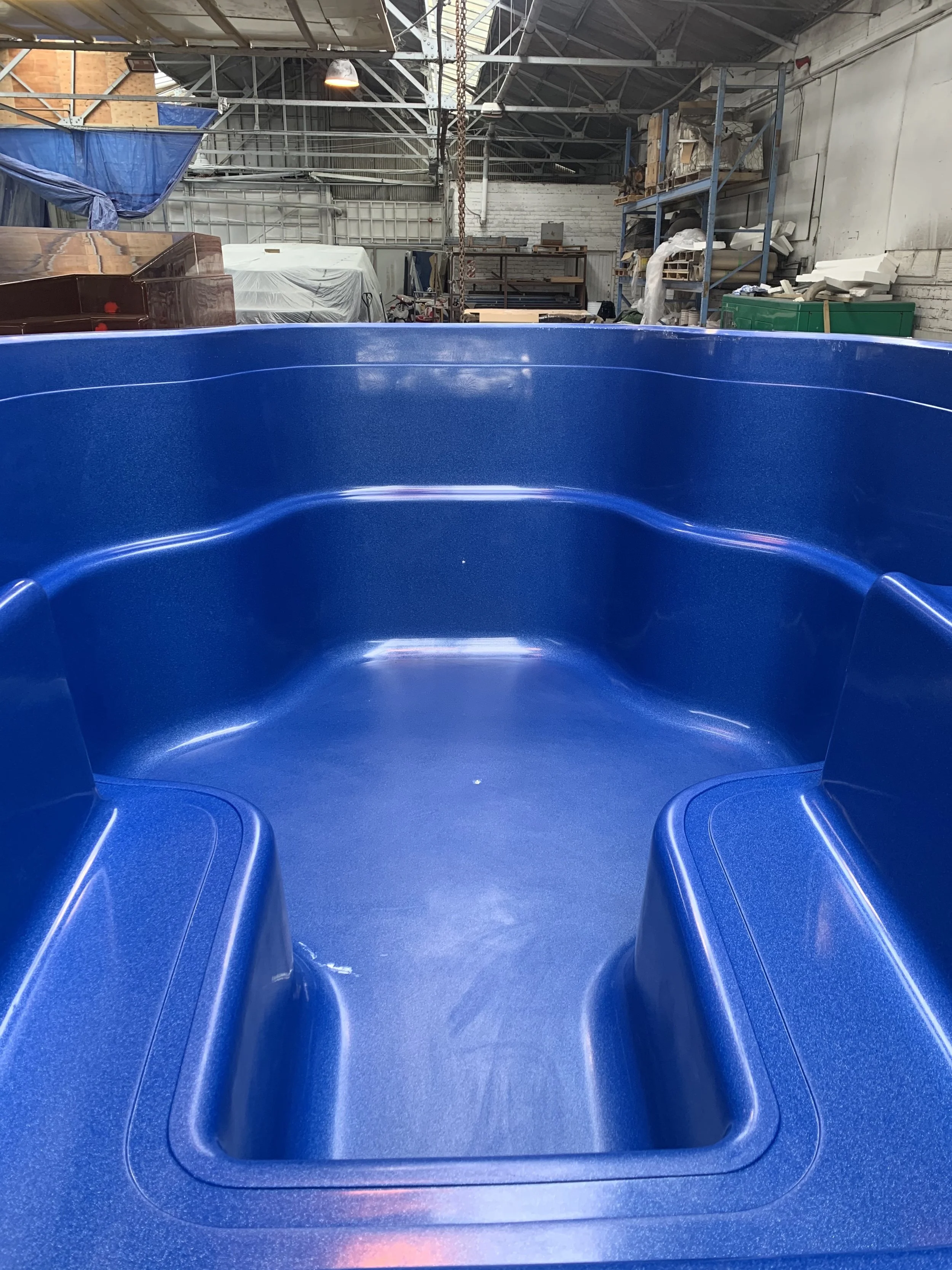Interior of a large, blue, inflatable boat with built-in seats, inside a workshop with various equipment and supplies in the background