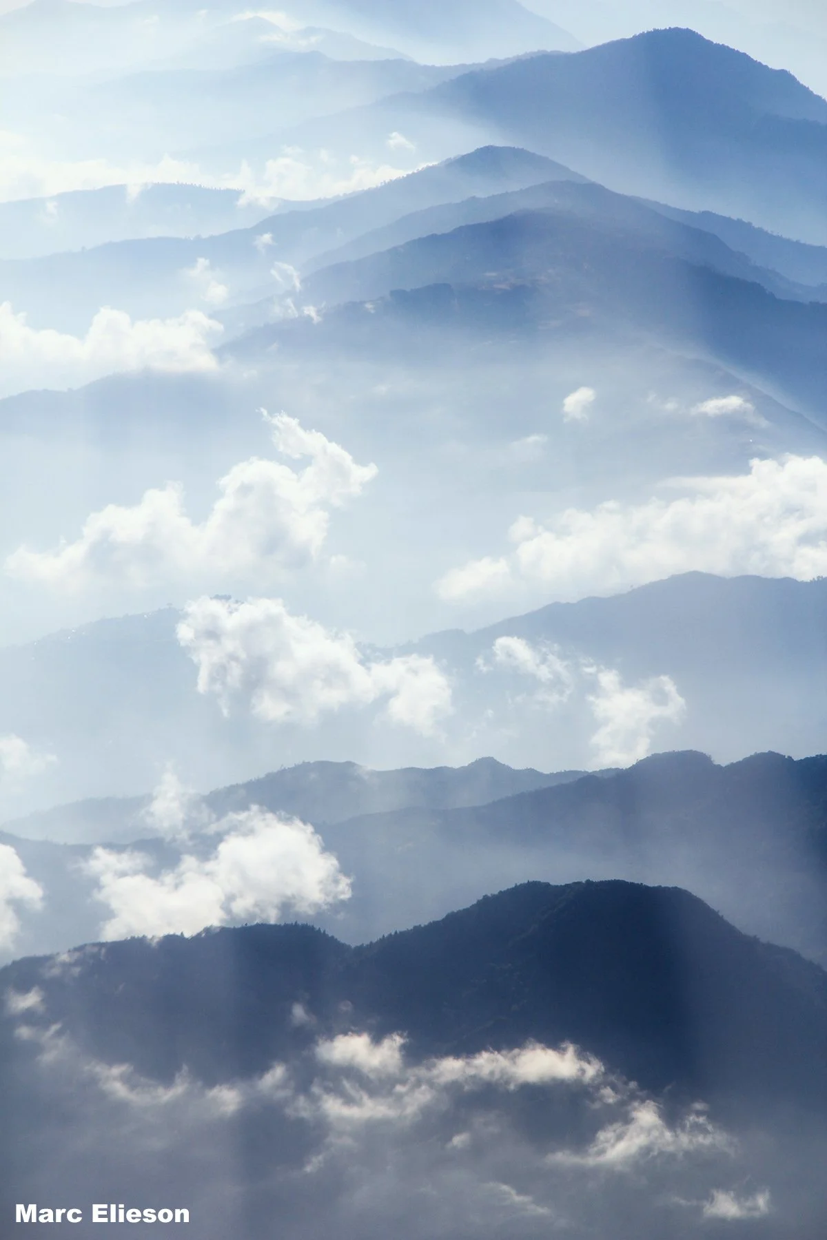 Multiple mountain ranges covered in mist, with clouds in the sky.