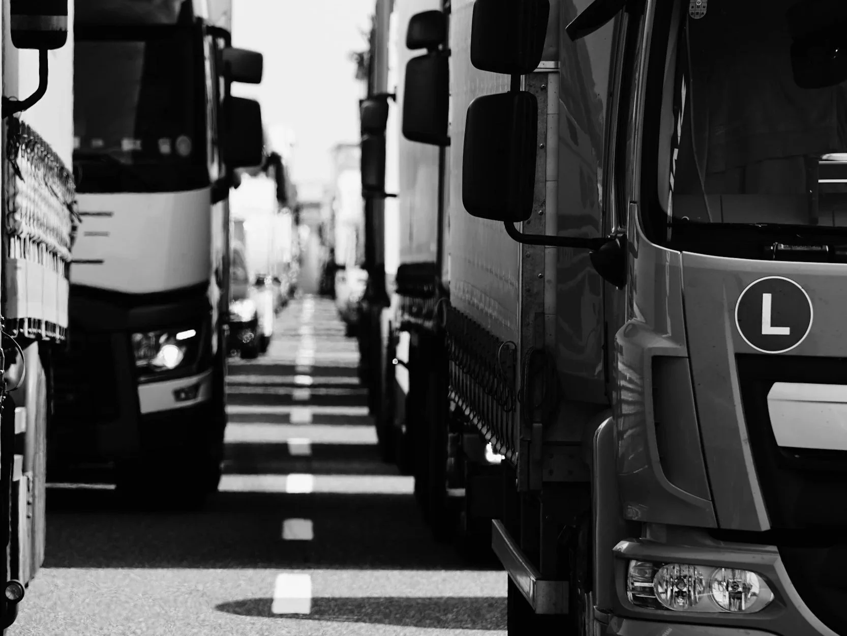 Black and white photo of a narrow street filled with parked trucks lined up on both sides.