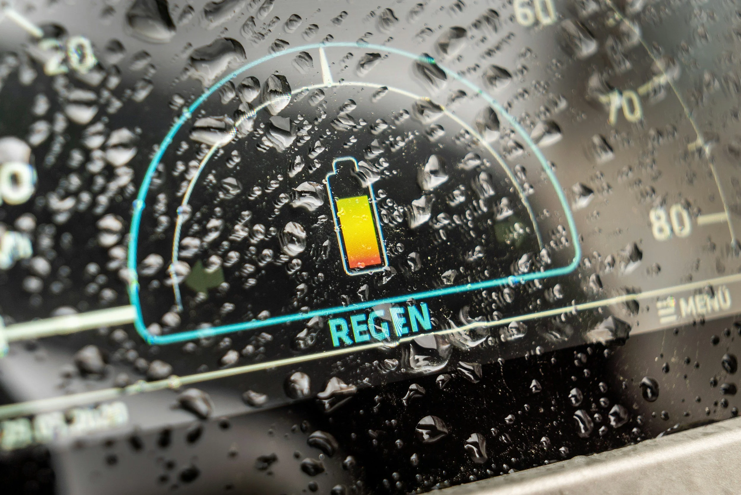 Close-up of a car dashboard display with a water droplet-covered surface showing a low battery level and the word 'REGEN'.