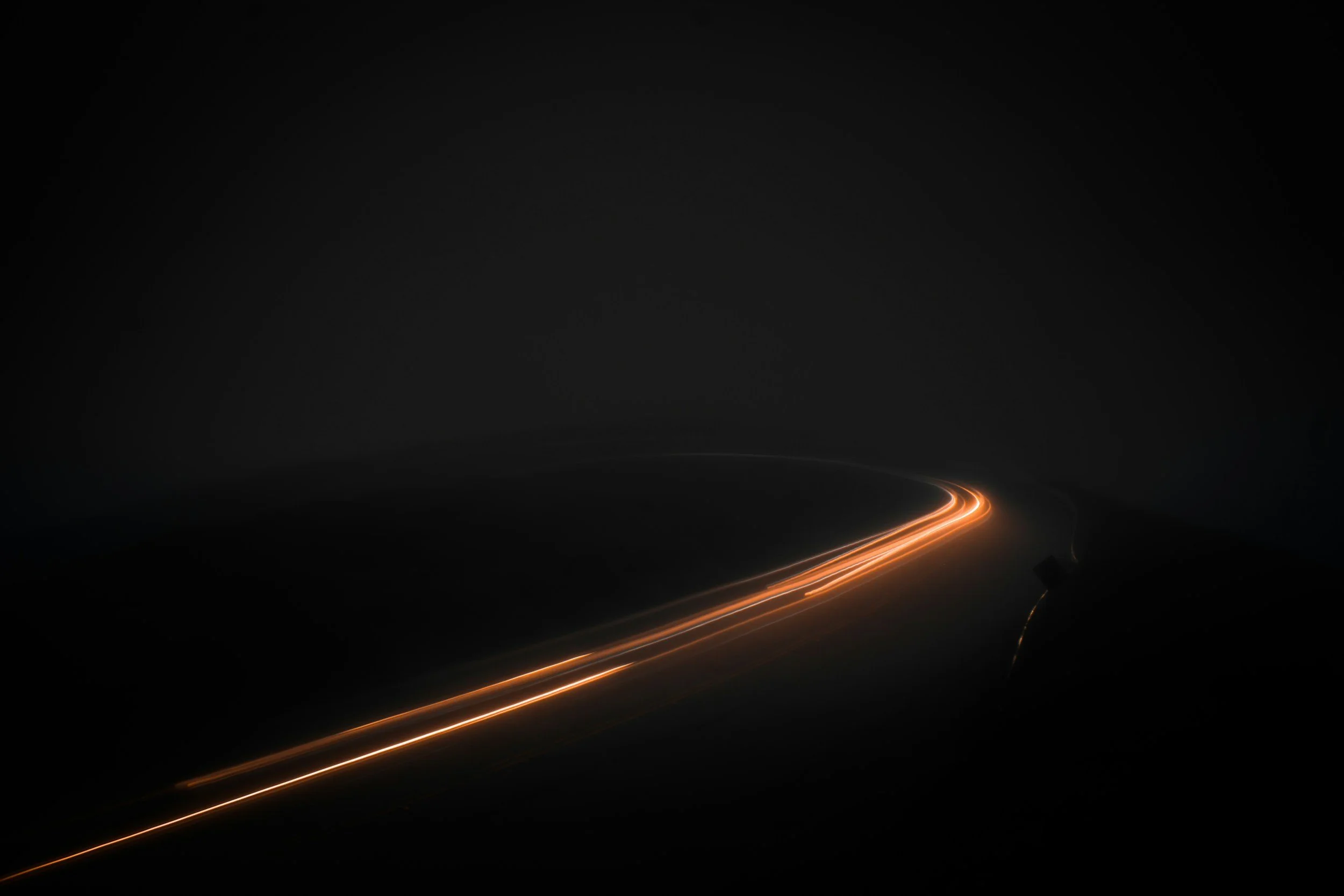 Nighttime view of a winding road with streaks of light from moving vehicles, surrounded by darkness.