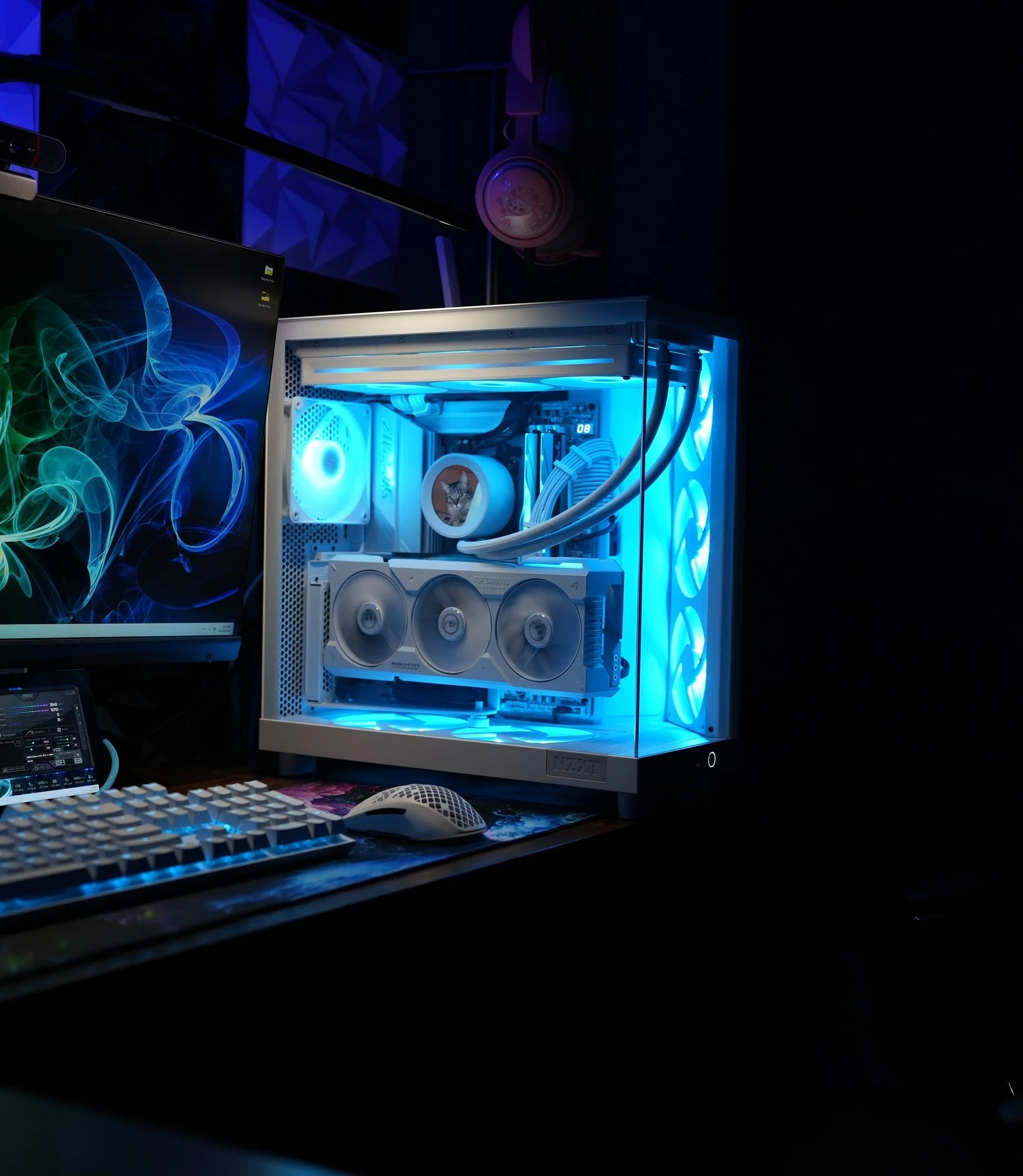 A custom-built gaming computer with a white case, illuminated by blue LED lights, placed on a desk next to a monitor, keyboard, and mouse.