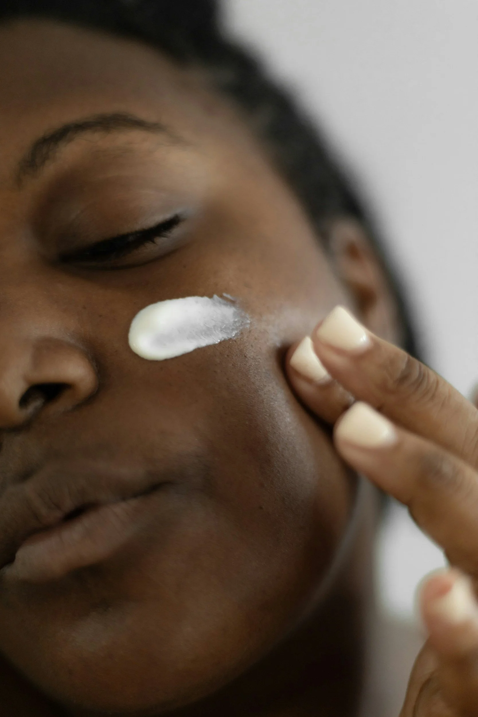 Black woman applying skincare cream or moisturizer on her cheek.